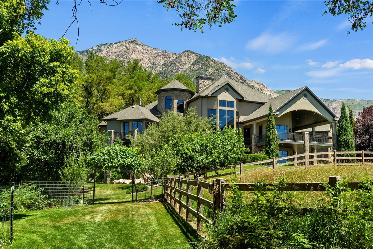 Lower Orchard, featuring fruit trees & bushes. Mountain backdrop with a multi-level residence featuring a stone-clad turret and expansive windows
