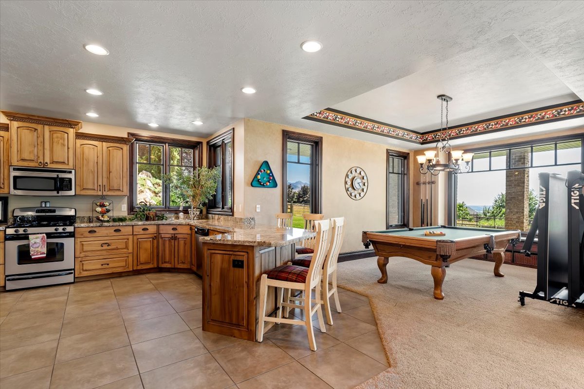 Open-concept kitchen and recreation area featuring warm wood cabinetry, stainless steel appliances, granite countertops, and tile flooring