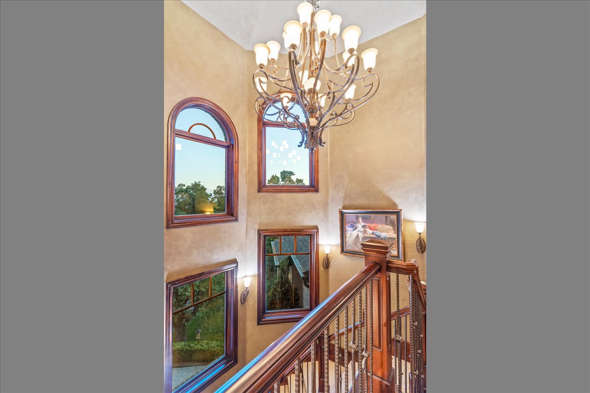 Architectural staircase featuring a wrought iron chandelier, multiple arched and rectangular windows with wood framing, and wood handrails with decorative balusters