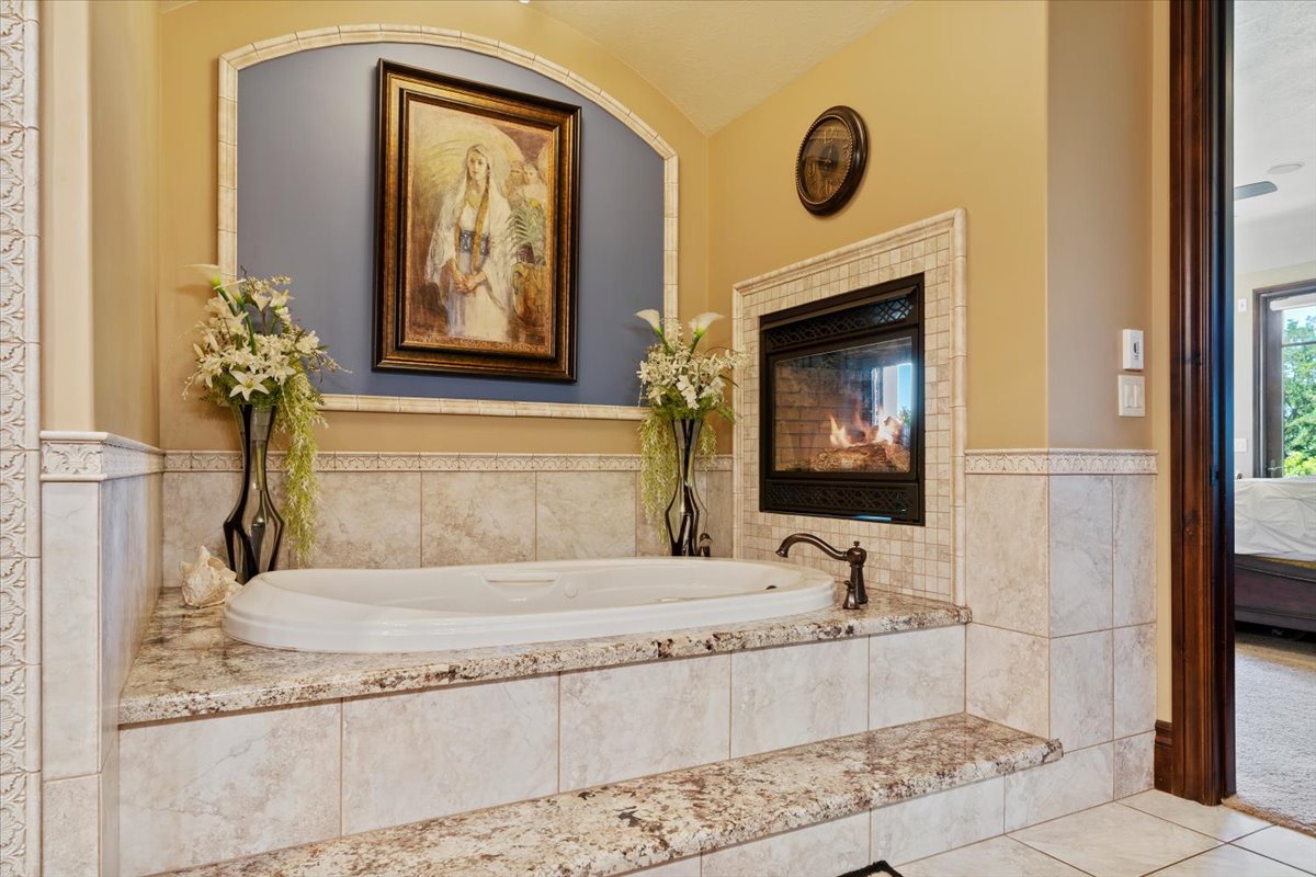 Built-in jetted tub with tile surround and stone countertop, complemented by an integrated fireplace with a tile hearth