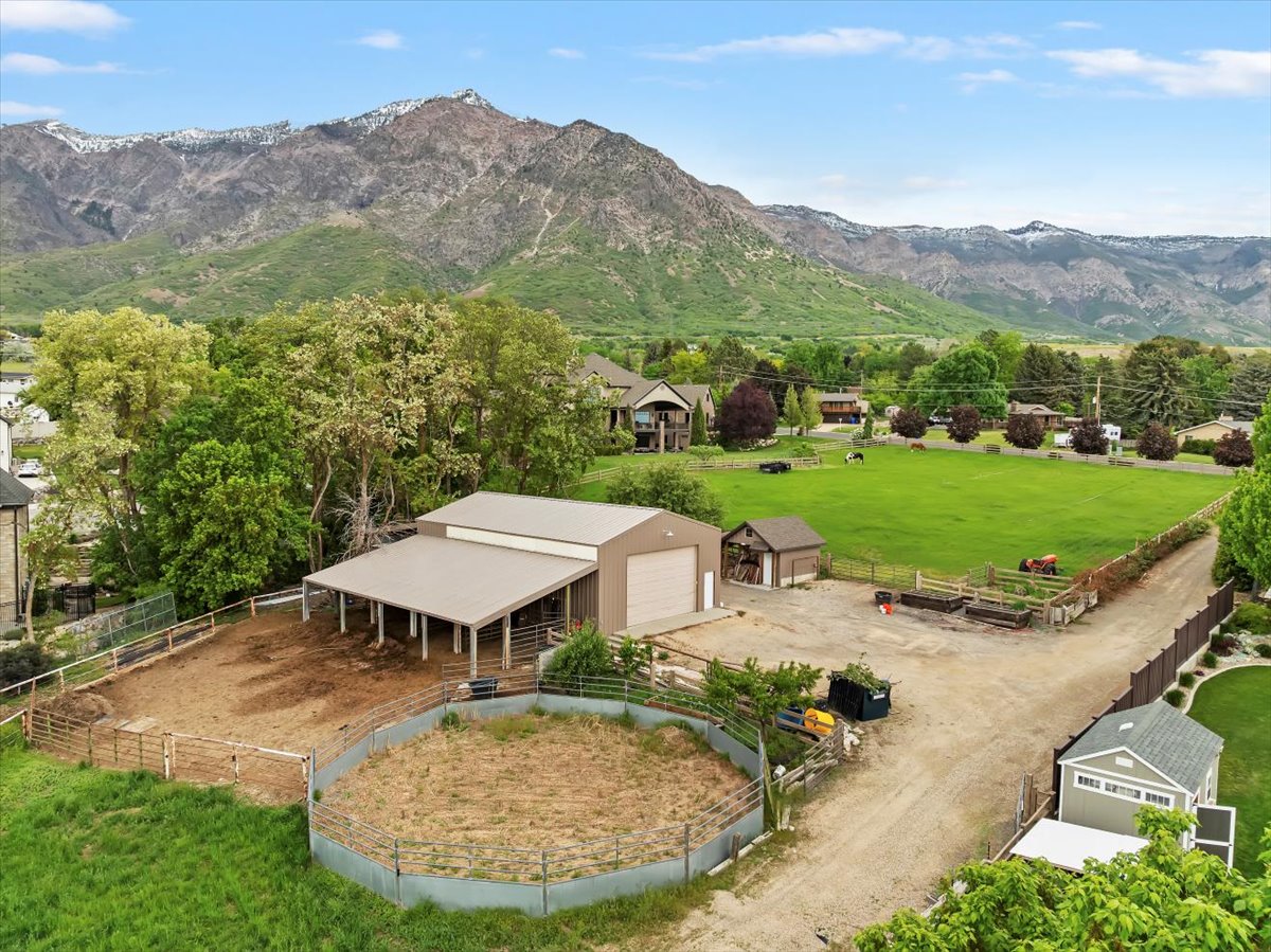 Expansive property featuring a large barn with covered stalls and two garage doors, a fenced riding pen, and a secondary outbuilding