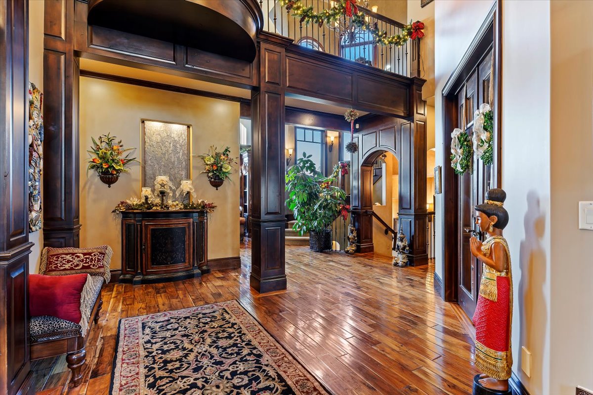 Grand entryway featuring rich wood-finish flooring, dark wood-paneled archways, and a two-story ceiling with an upper-level balcony