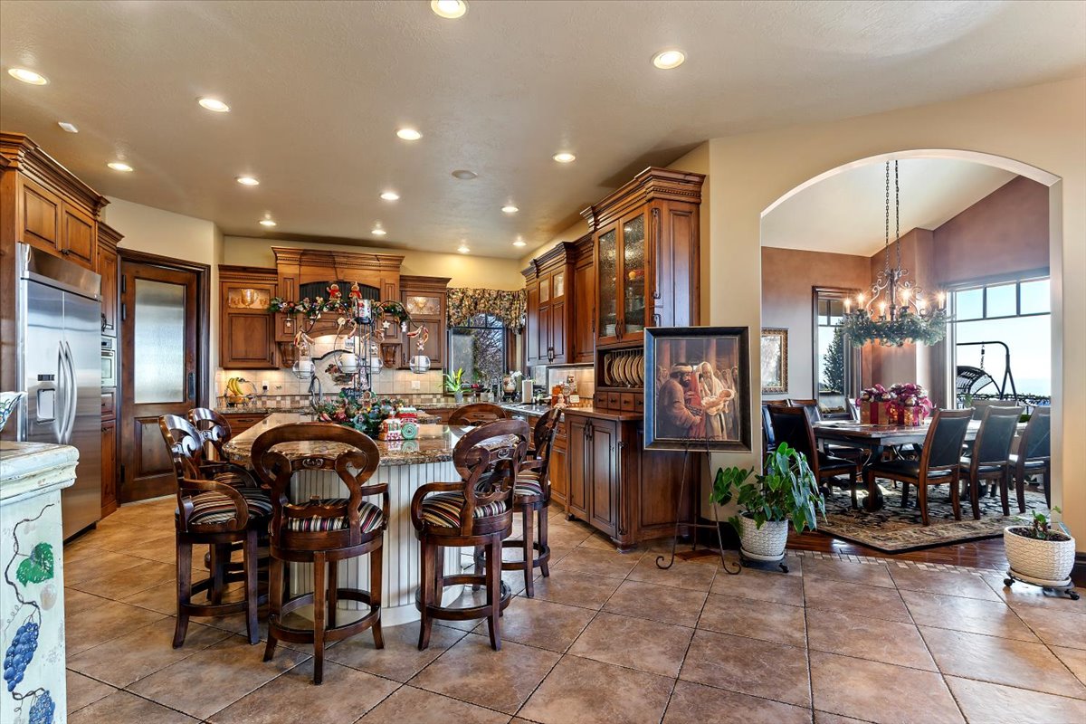 Spacious kitchen featuring extensive wood cabinetry, stainless steel refrigerator, recessed lighting, a central island with integrated seating, and large tile flooring