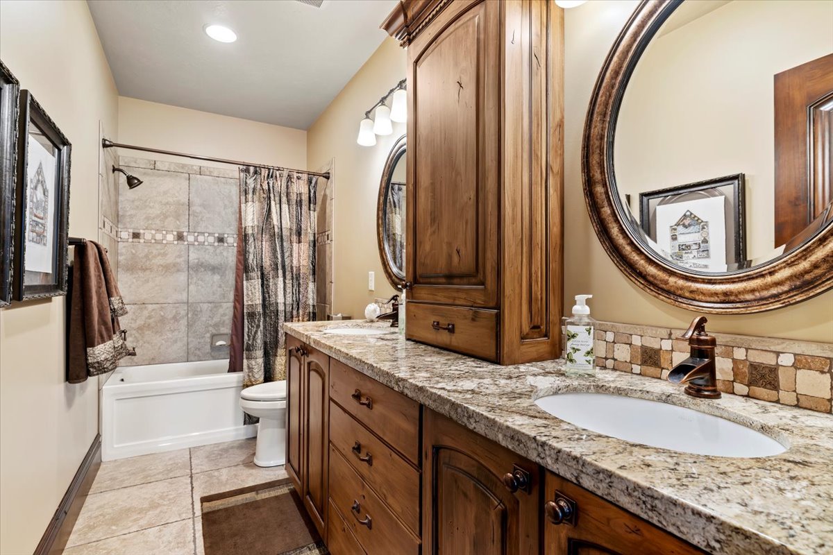 Bathroom featuring a dual vanity with wood cabinetry, granite-finish countertops, and under-mount sinks