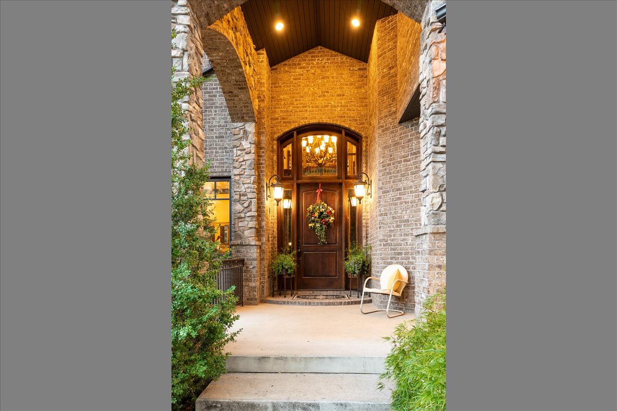 Grand entryway featuring a dark wood door with an arched transom, flanked by brick and stone veneer