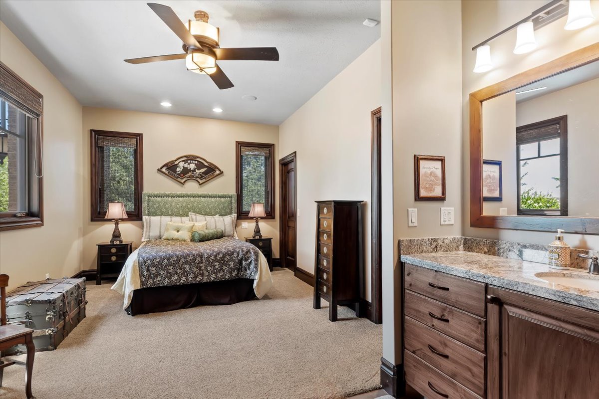 Carpeted bedroom with multiple dark-framed windows, a ceiling fan, recessed lighting, and an attached vanity featuring a granite countertop, undermount sink, and wood-finish cabinetry
