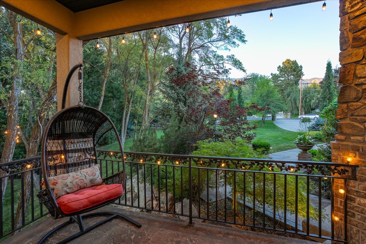 Covered balcony featuring a decorative wrought iron railing, string lighting, and a stone-clad exterior wall