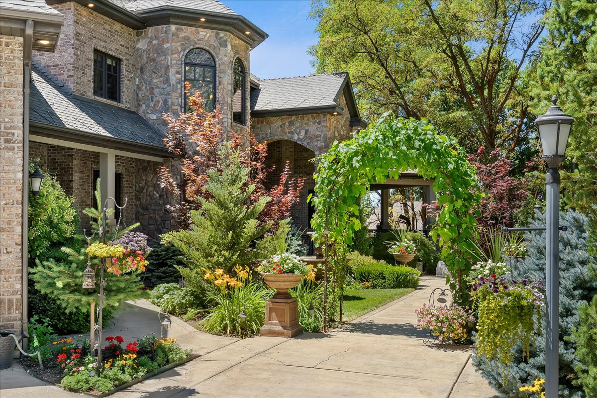 Stone and brick exterior with arched windows, a covered entryway, and a vine-covered archway over a paved path