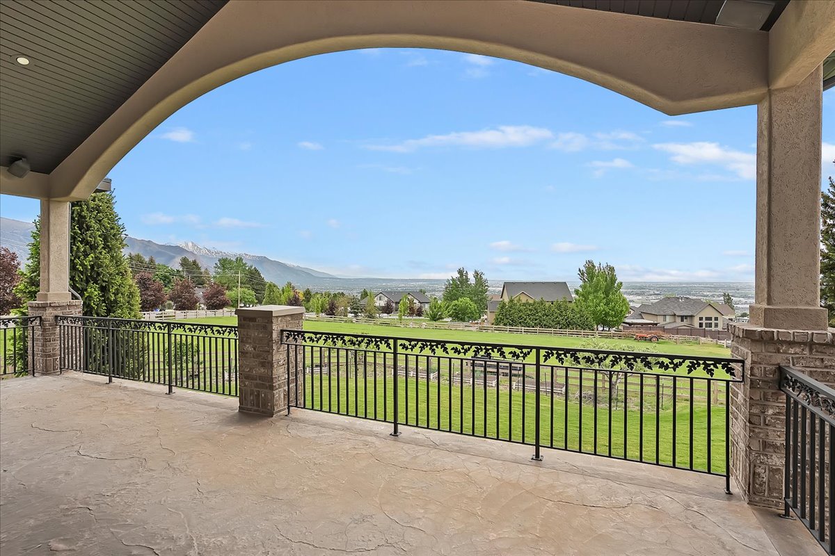 Expansive covered patio featuring stamped concrete flooring, decorative wrought iron railing, brick pillars, and a mountain backdrop