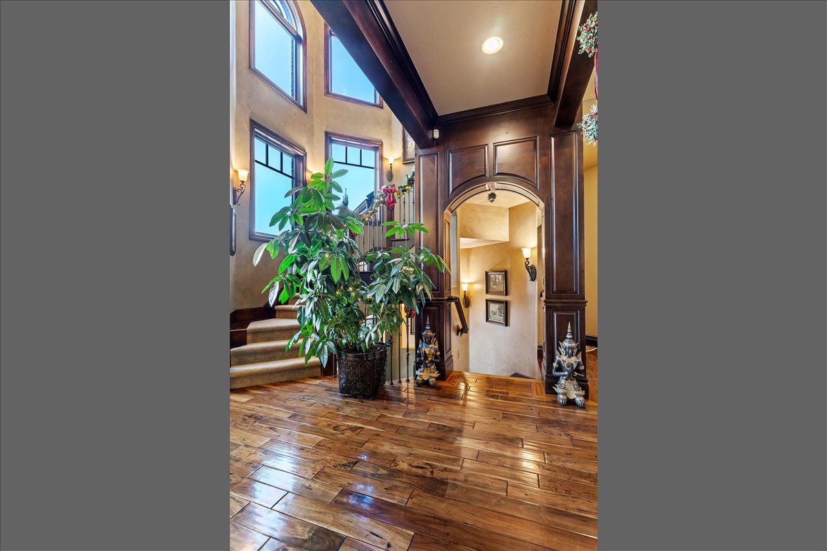 Entryway featuring wood-finish flooring, a carpeted staircase with dark iron balusters, arched dark wood trim, wall paneling, and multiple windows