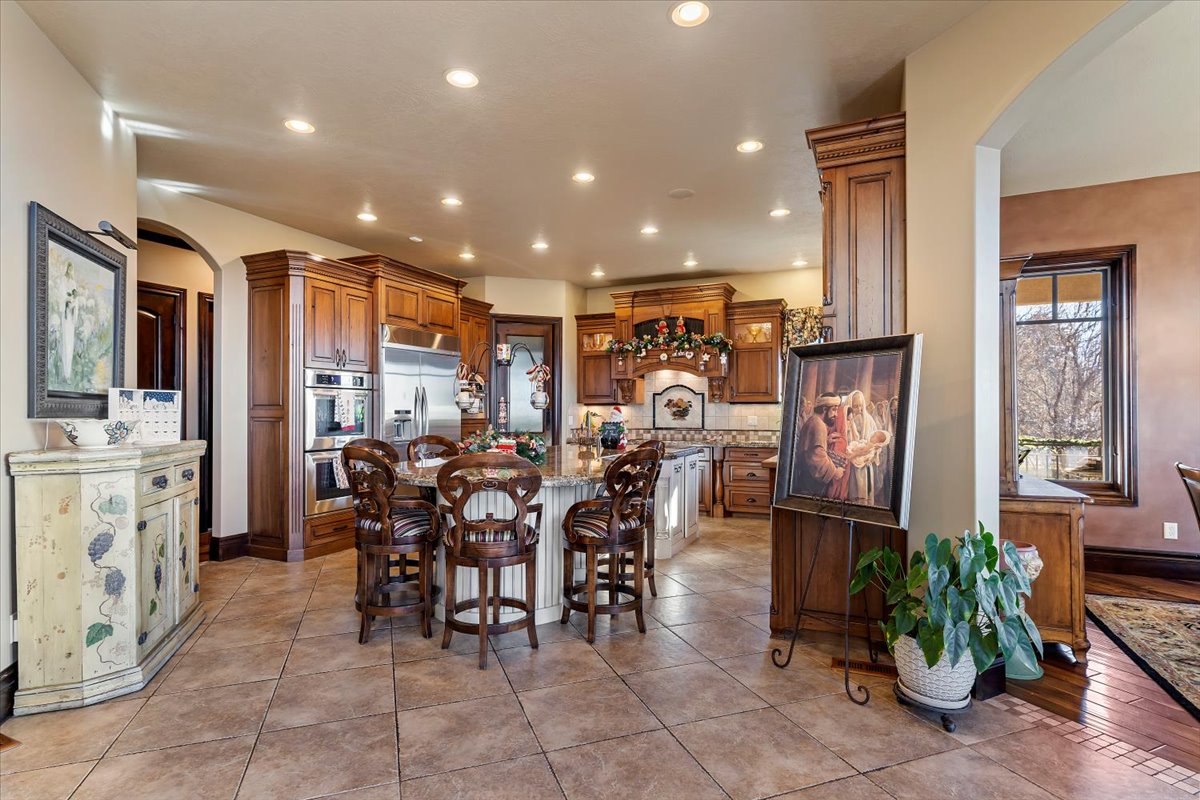 Spacious kitchen featuring warm wood cabinetry, stainless steel appliances, a central island with seating, recessed lighting, and tile flooring