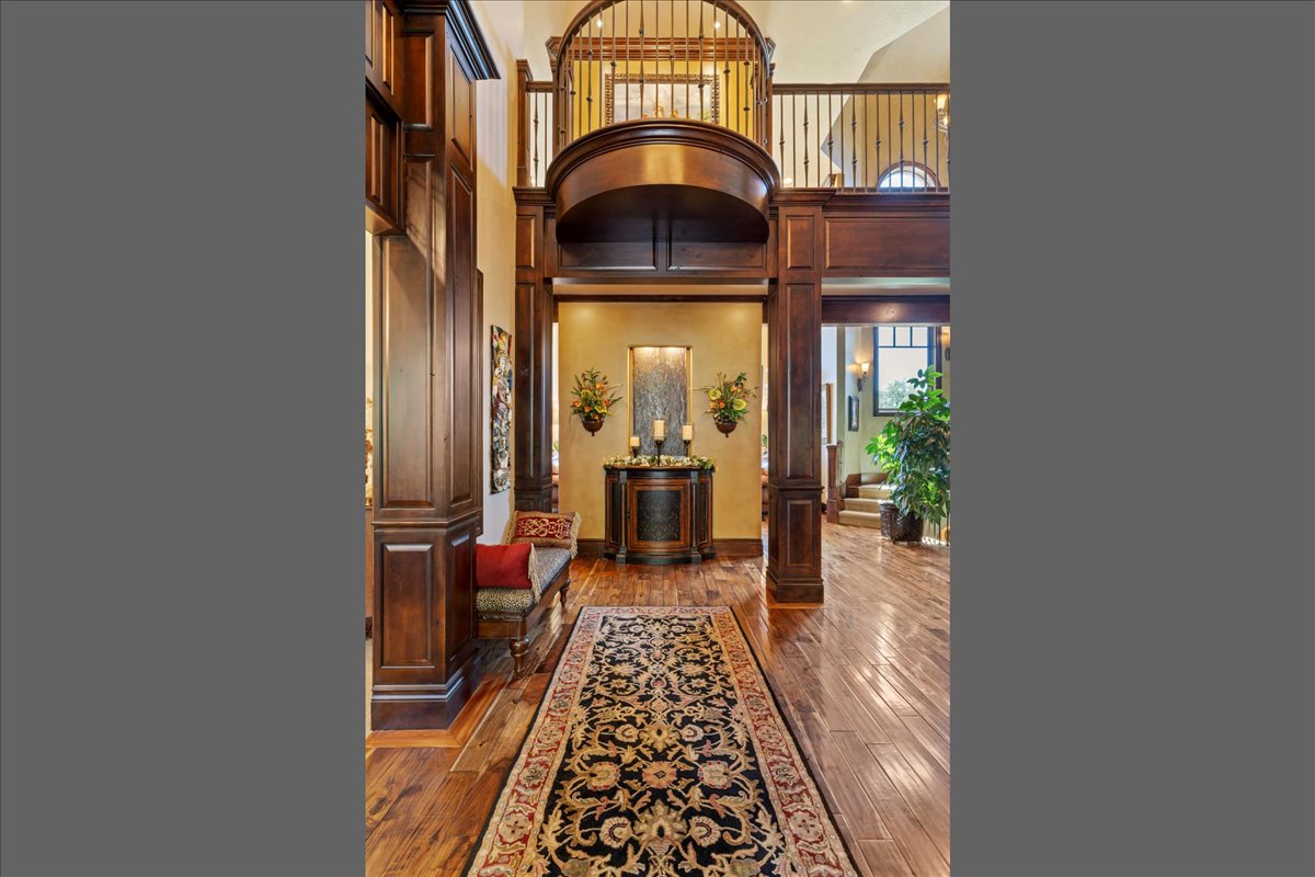 Grand foyer featuring rich wood-finish flooring, an ornate overhead balcony, decorative wood paneling, and a built-in console table