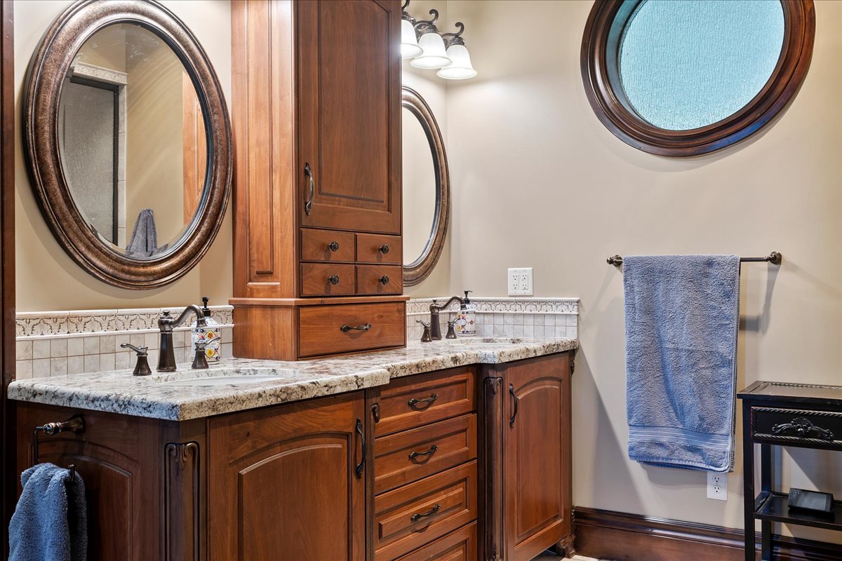 Dual vanity with wood-finish cabinetry, stone countertops, and bronze-finish fixtures