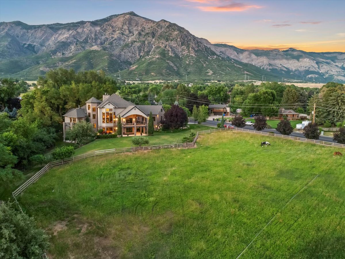 Expansive green acreage with a four-rail fence and a distant mountain backdrop