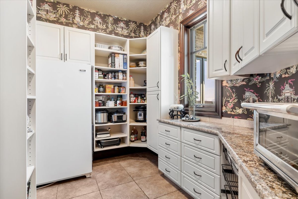 Kitchen pantry featuring extensive white cabinetry, a built-in refrigerator, corner shelving, and a window with wood trim