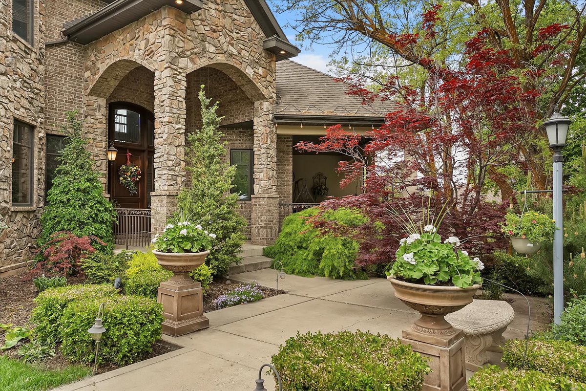 Stone and brick facade with arched entryways, a dark wood entry door, and a concrete pathway