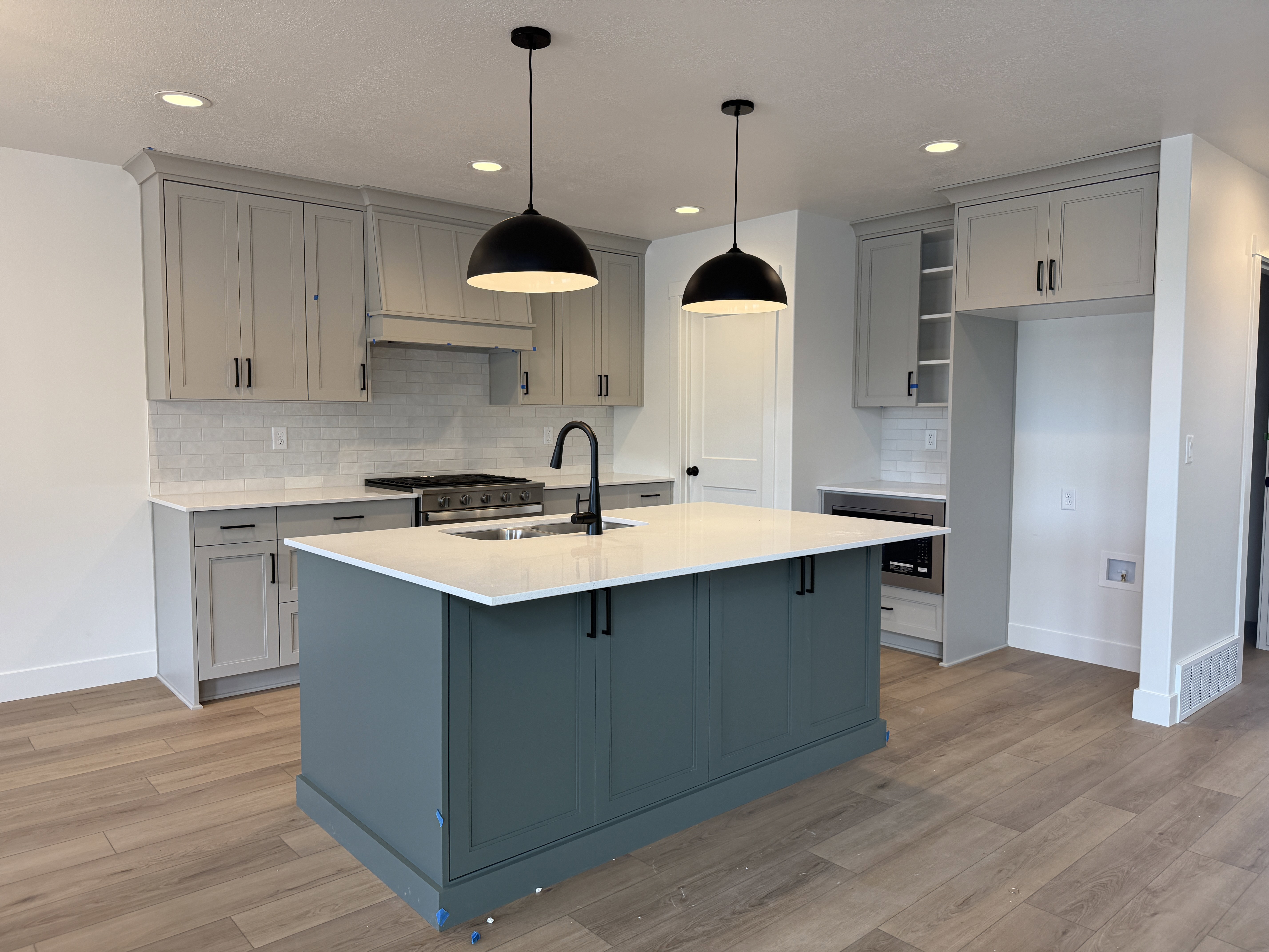 Kitchen featuring a central island with a contrasting deep teal finish, light gray cabinetry, and a white subway tile backsplash