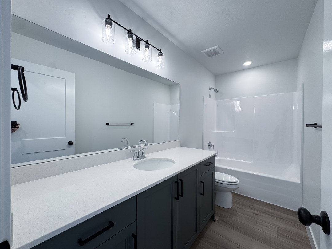 Bathroom vanity featuring a light-toned countertop with an undermount sink, dark cabinetry, and black hardware