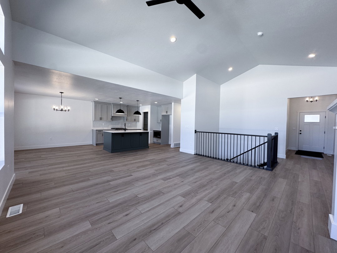 Open-concept living space featuring wood-finish flooring, vaulted ceilings with recessed lighting, and a kitchen with an island