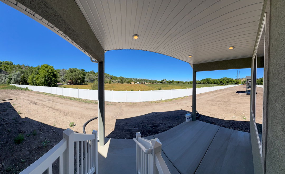 Covered concrete patio with recessed lighting, white railing, and a vinyl privacy fence enclosing the backyard