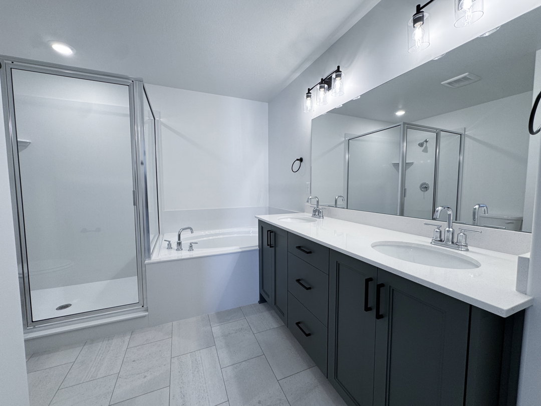 Contemporary bathroom featuring a spacious dual vanity with dark cabinetry and light countertops, a walk-in shower with clear glass enclosure, a separate built-in bathtub, and large format tile flooring