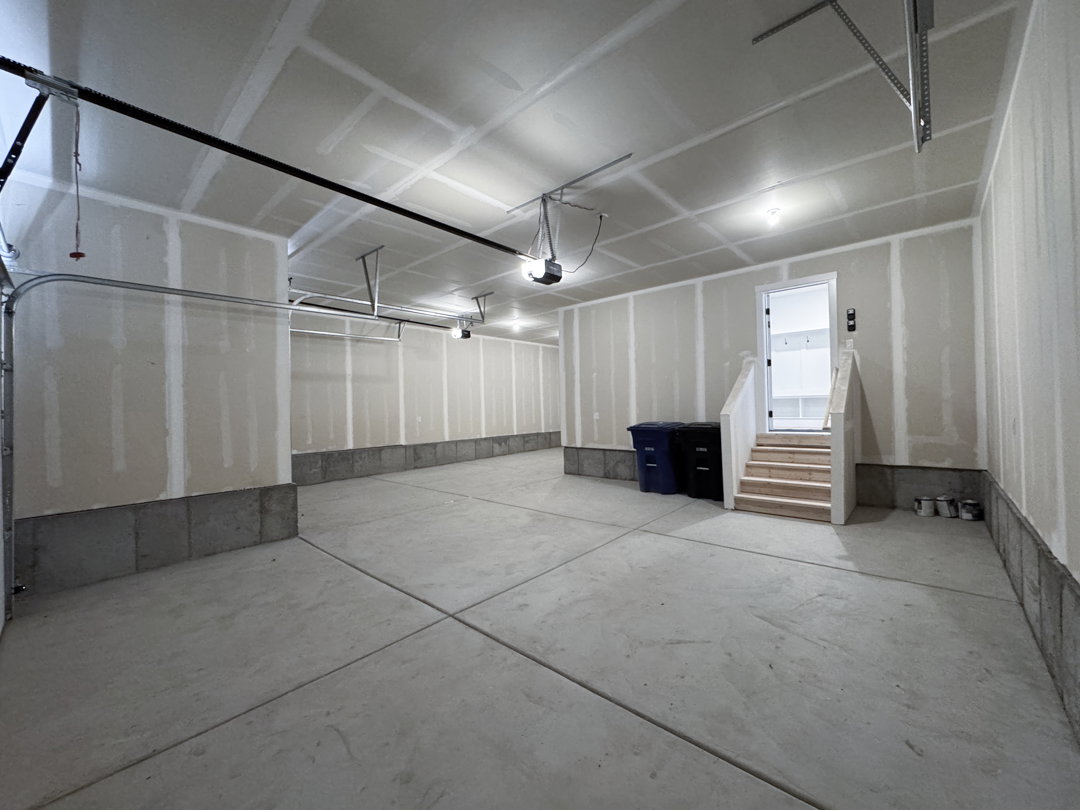 Spacious two-car garage featuring a concrete floor, unpainted drywall, and an interior access door with a short staircase