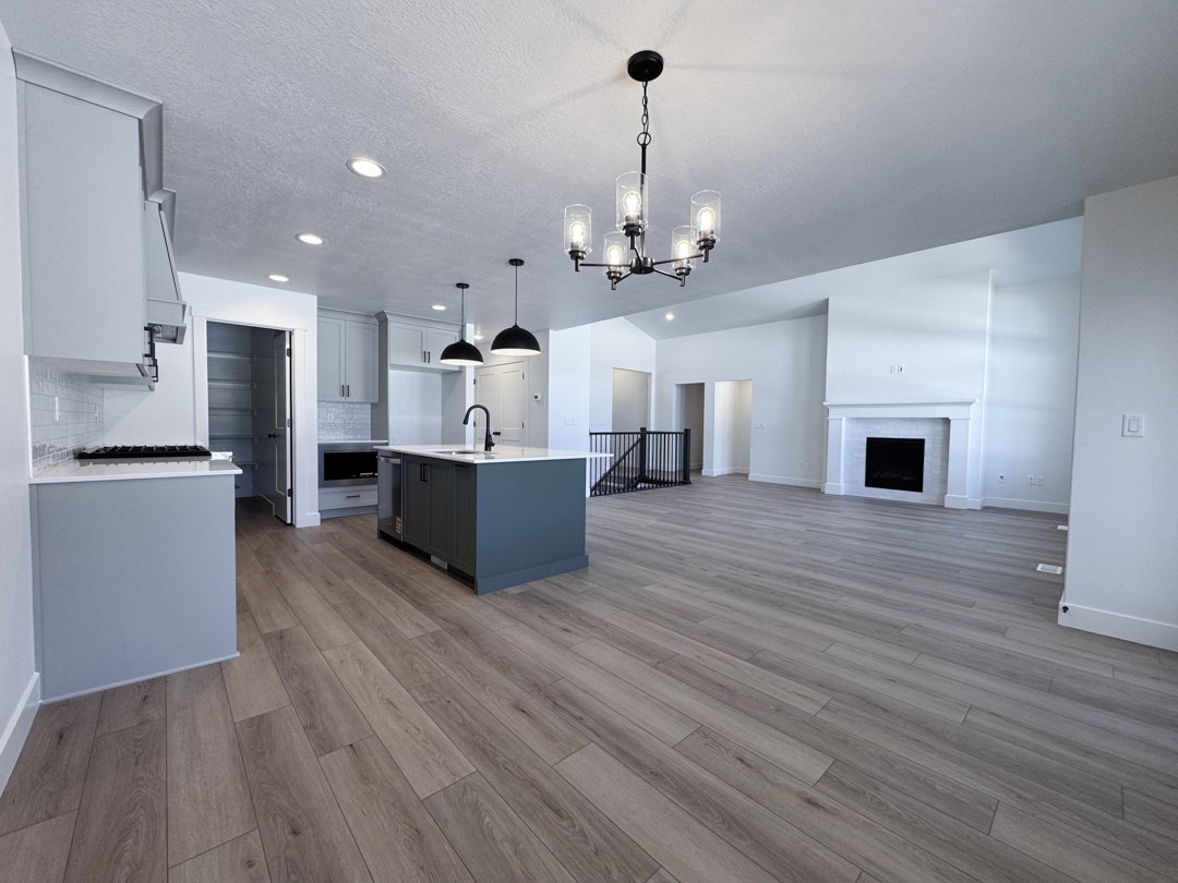 Open-concept living area featuring wood-finish flooring, a kitchen island with seating, a built-in fireplace, recessed lighting, and a modern chandelier