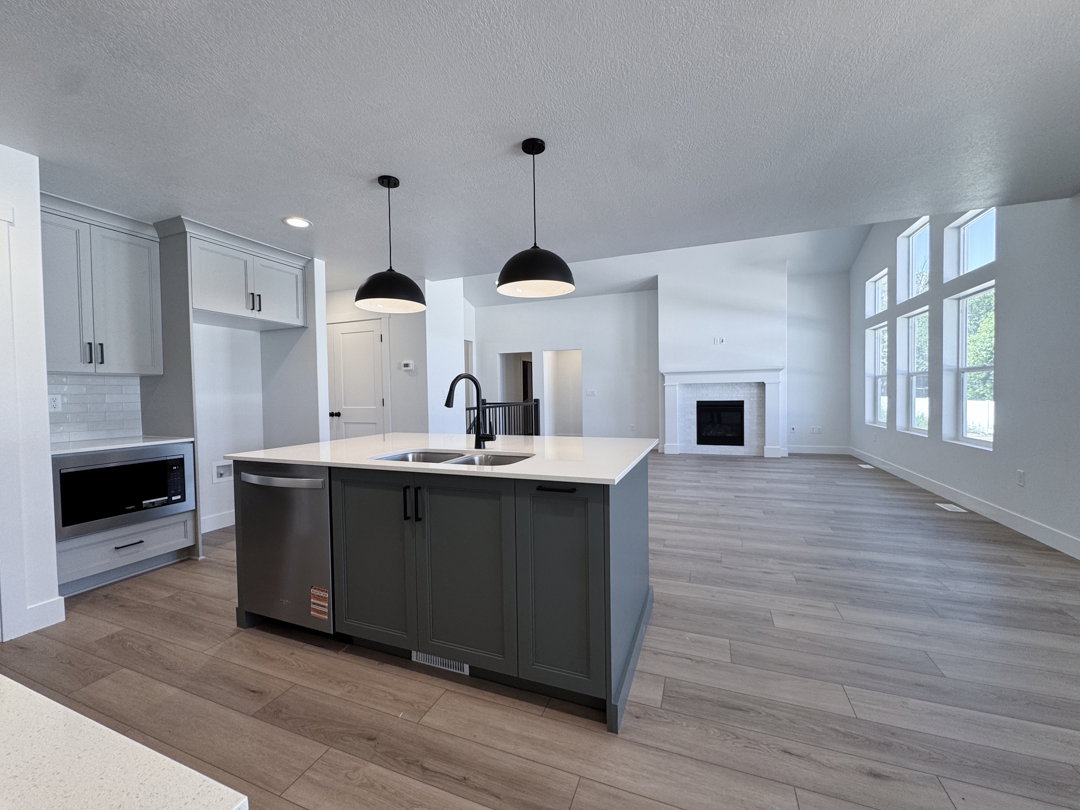 Open-concept kitchen and living area featuring a large center island with double sink, stainless steel dishwasher, and two pendant lights
