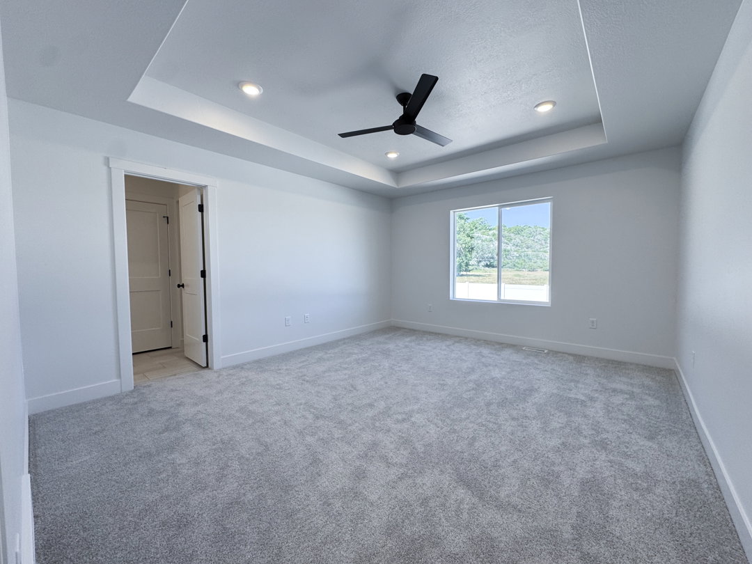 Spacious room featuring a tray ceiling with recessed lighting and a ceiling fan, light gray carpet flooring, white baseboards, and a large window