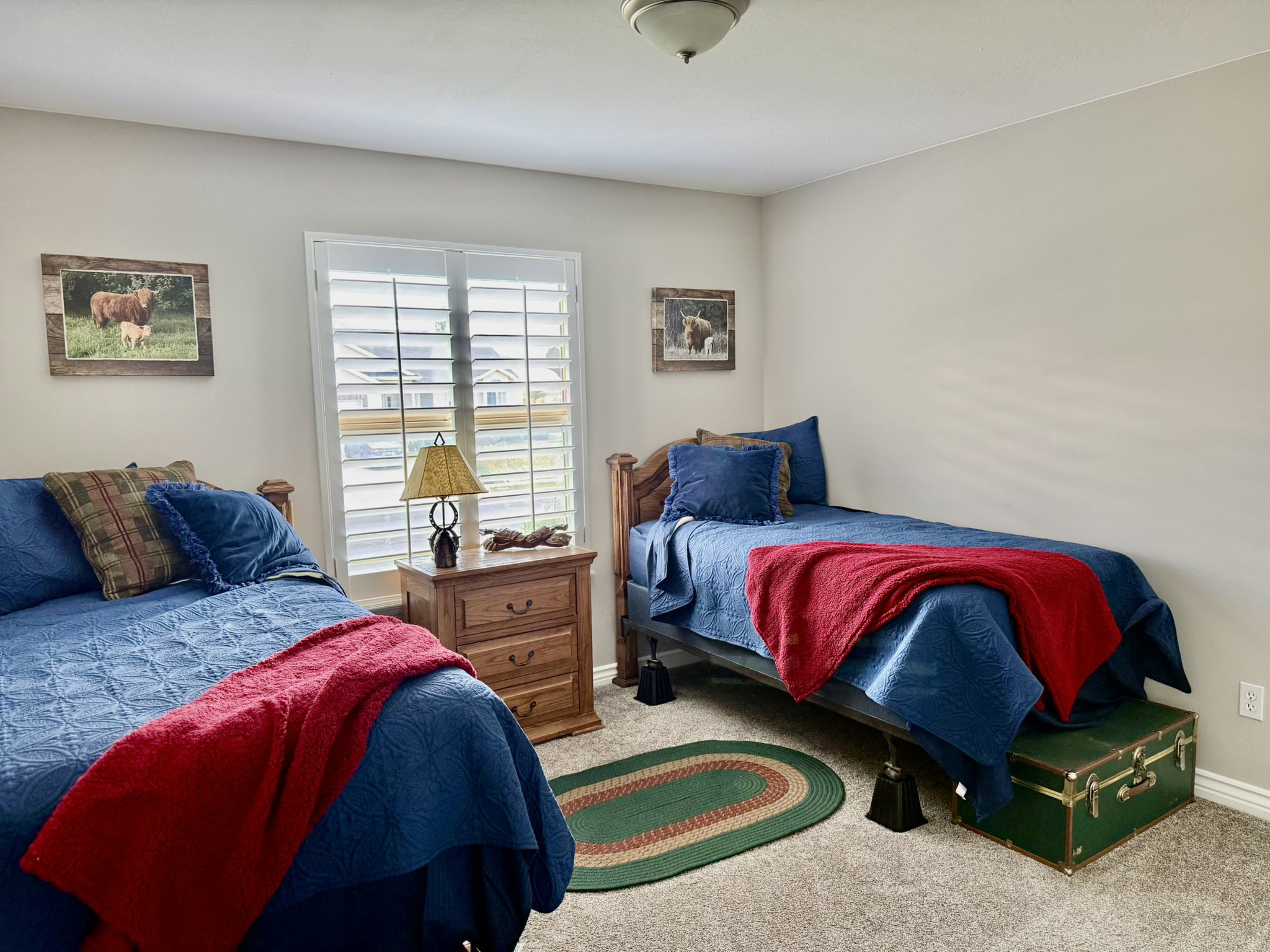 Carpeted room featuring a window with plantation shutters, a wood-finish nightstand, and neutral wall paint
