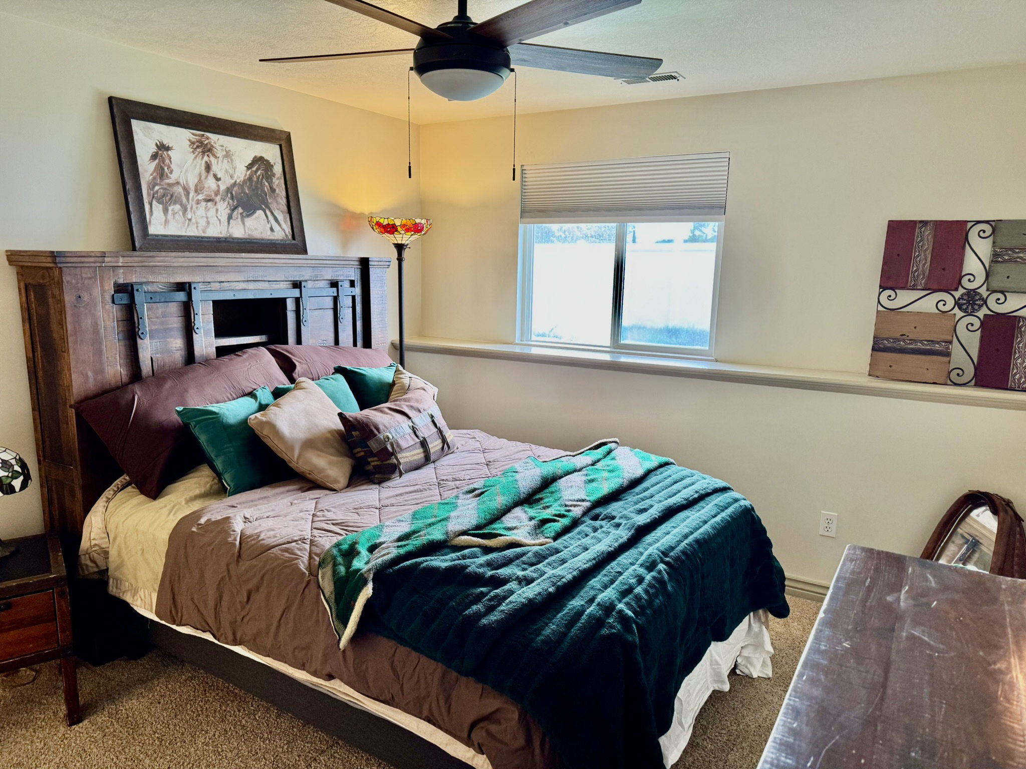 Bedroom featuring a wood-finish headboard with built-in shelving, textured carpet, and a ceiling fan with integrated lighting