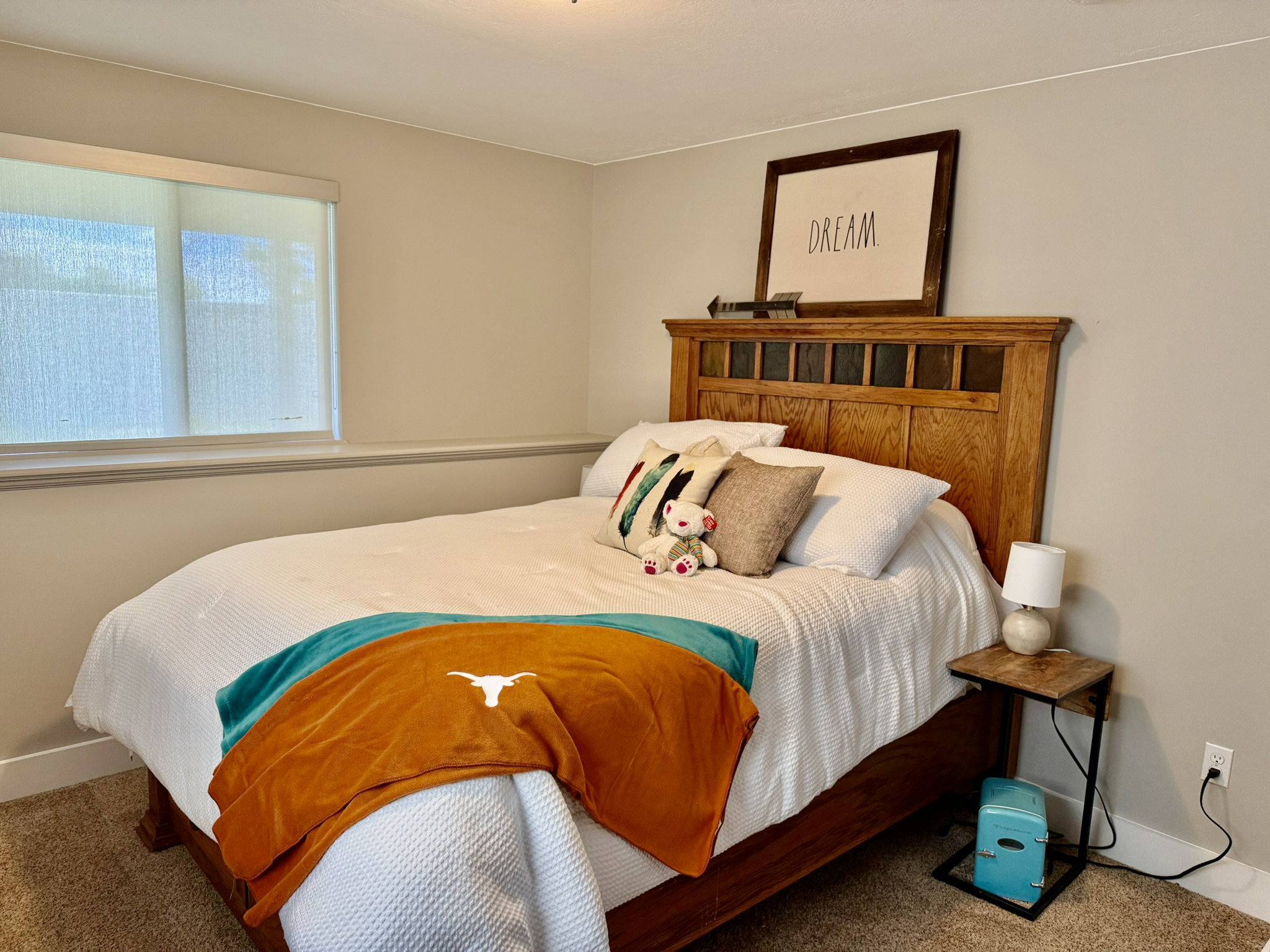 Bedroom featuring neutral wall paint, a large window with roller shades, and plush carpeting