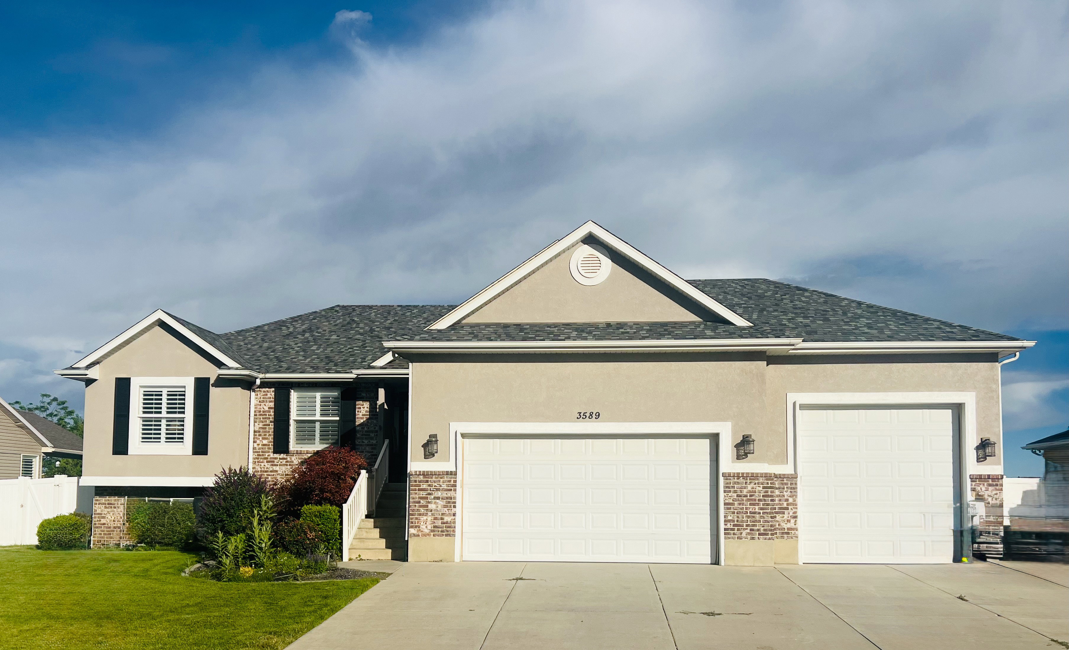 Multi-level stucco exterior featuring brick accents, dark shutters, and a two-car garage