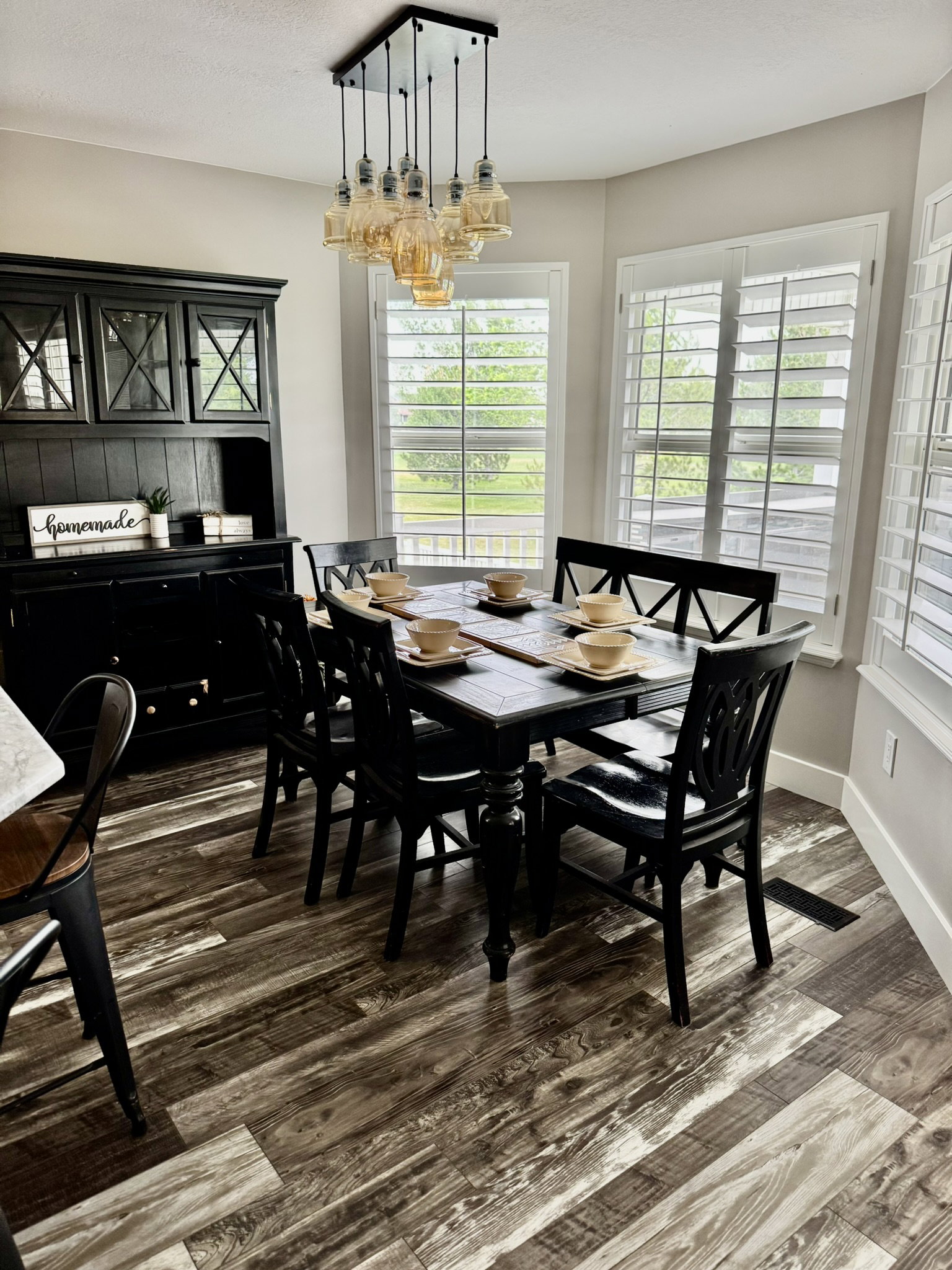 Dining area with wood-finish flooring, a contemporary multi-bulb chandelier, and multiple windows featuring plantation shutters