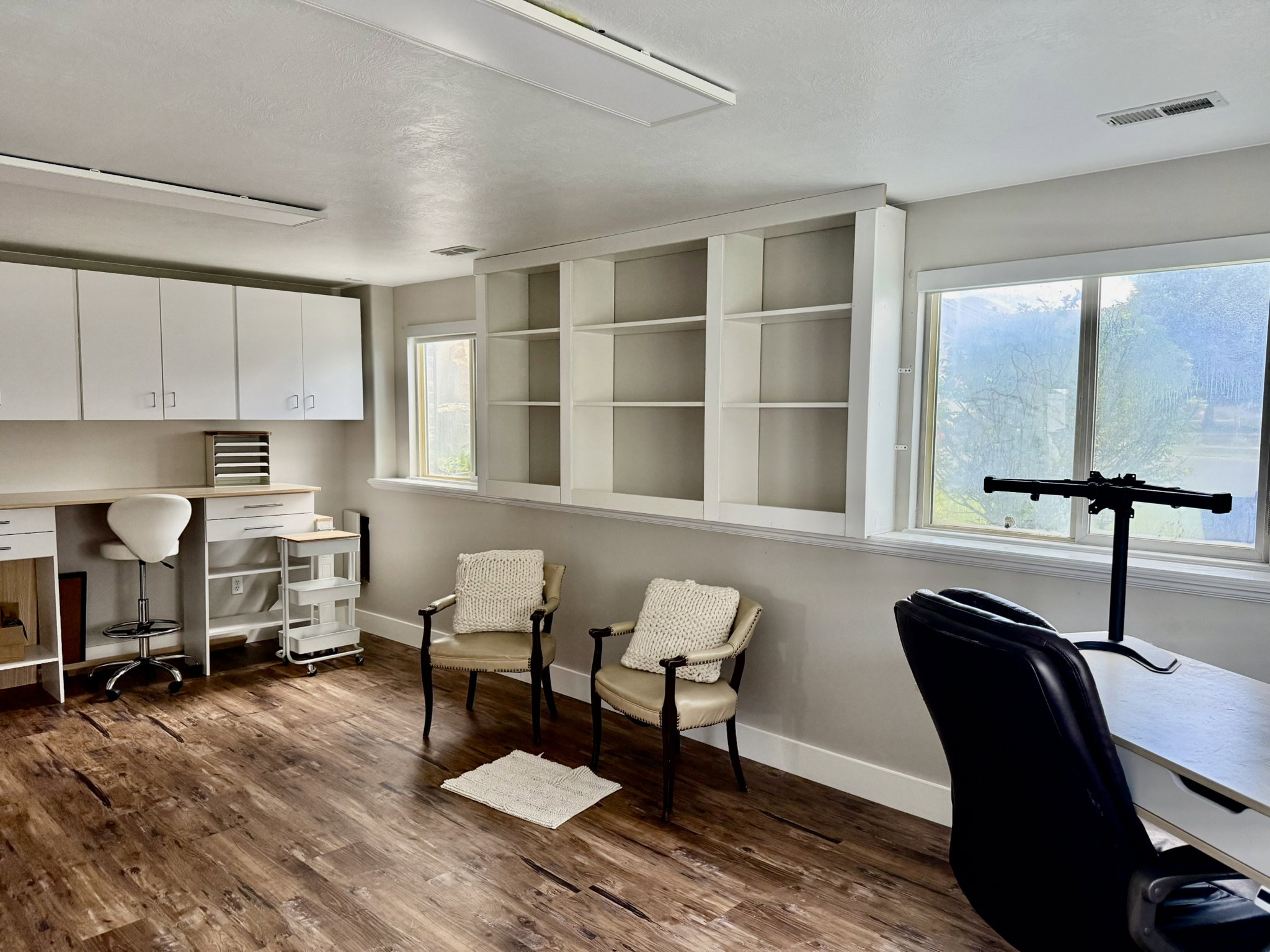 Spacious interior room featuring wood-finish flooring, built-in shelving, white cabinetry, and multiple windows