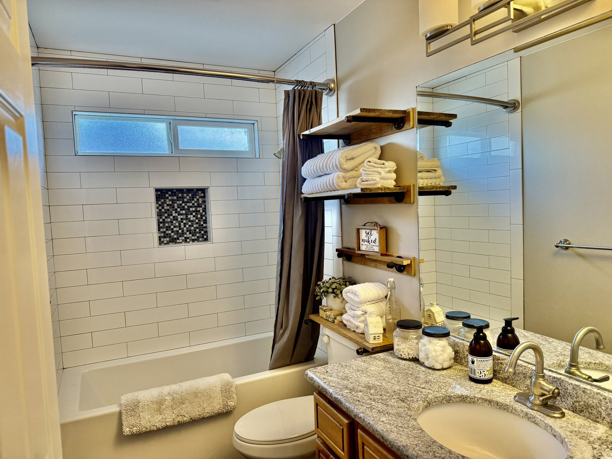 Bathroom featuring a tub and shower combination with white subway tile surround, an inset mosaic tile niche, and a horizontal window