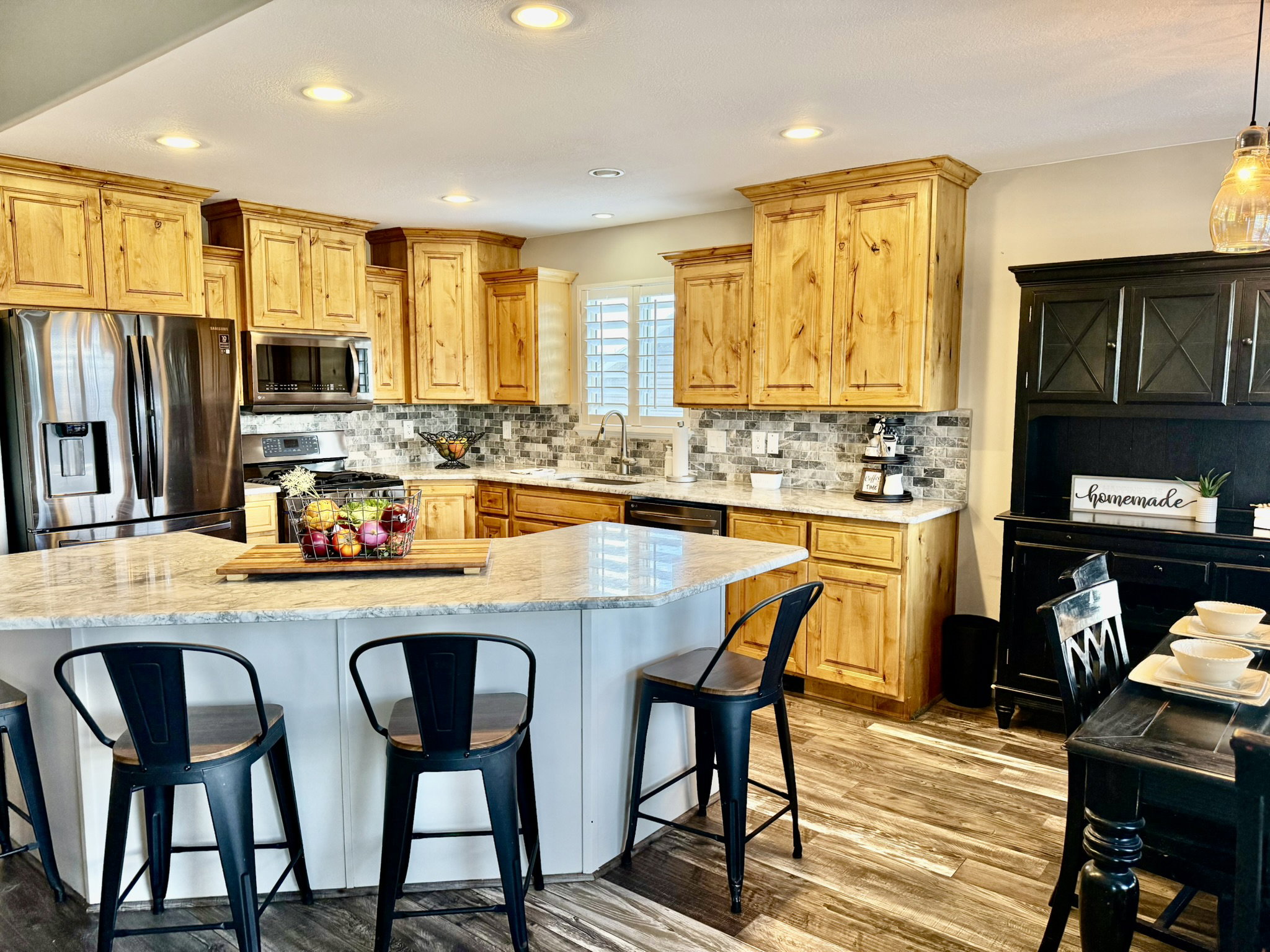 Well-appointed kitchen featuring light wood cabinetry, stainless steel appliances, a multi-tonal tile backsplash, and light-toned countertops