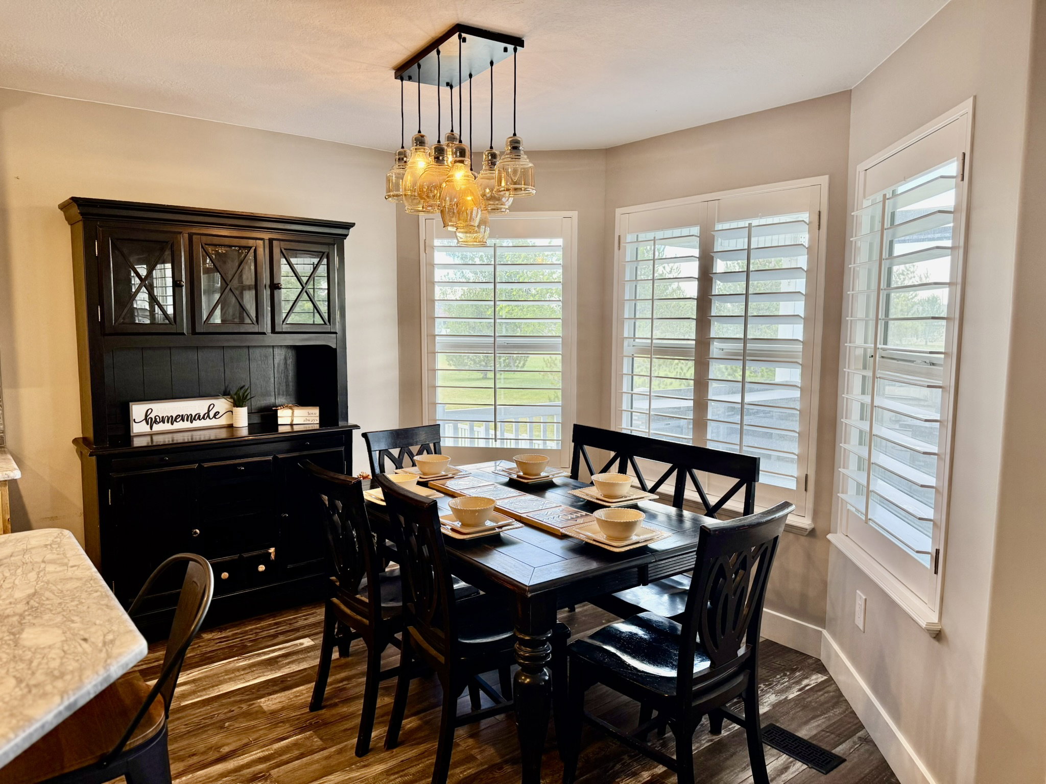 Dining area featuring wood-finish flooring, a contemporary multi-light pendant fixture, and a bay window configuration with white louvered shutters