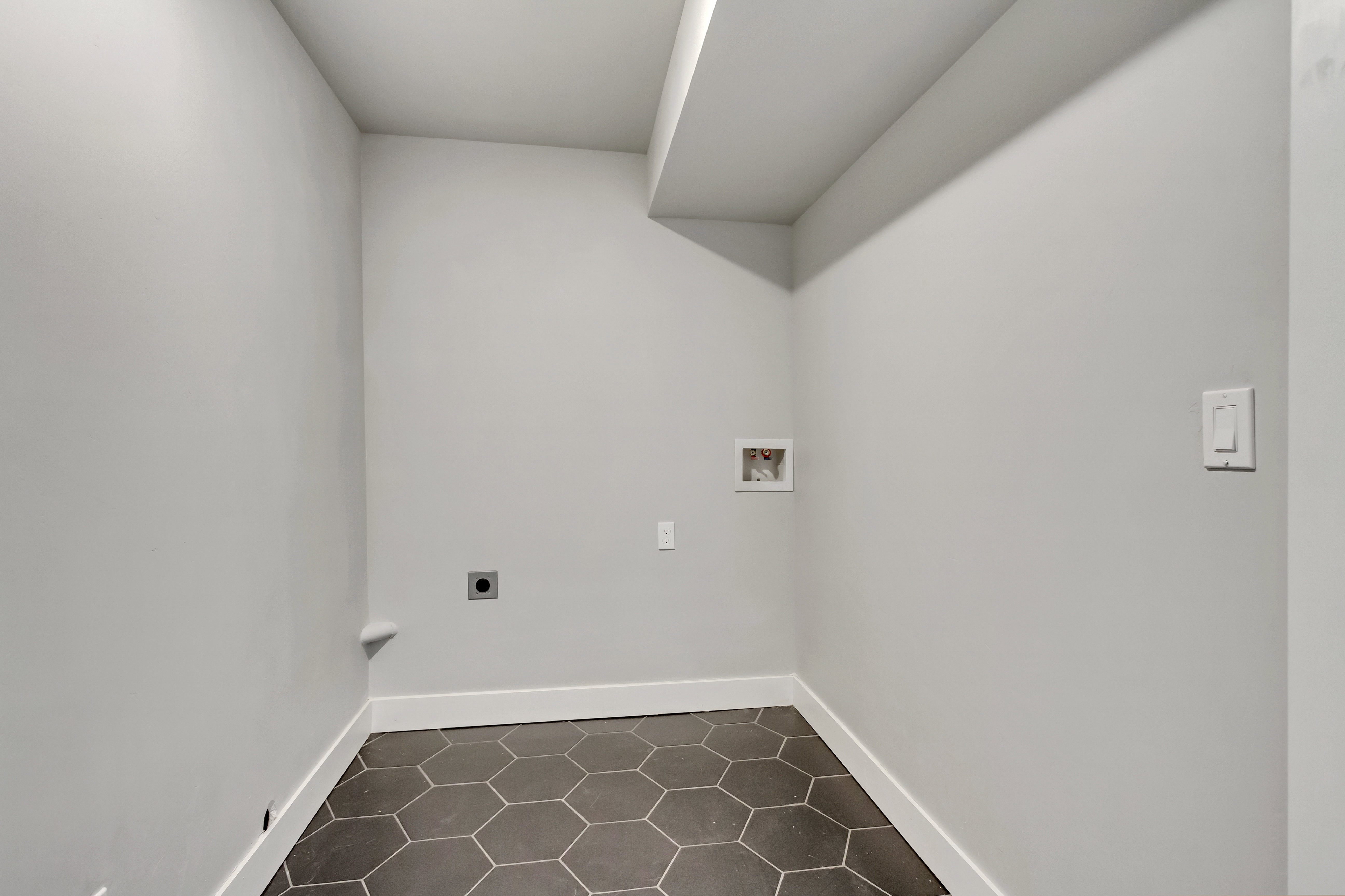Compact utility space featuring hexagonal floor tiles, light gray wall paint, and white baseboards