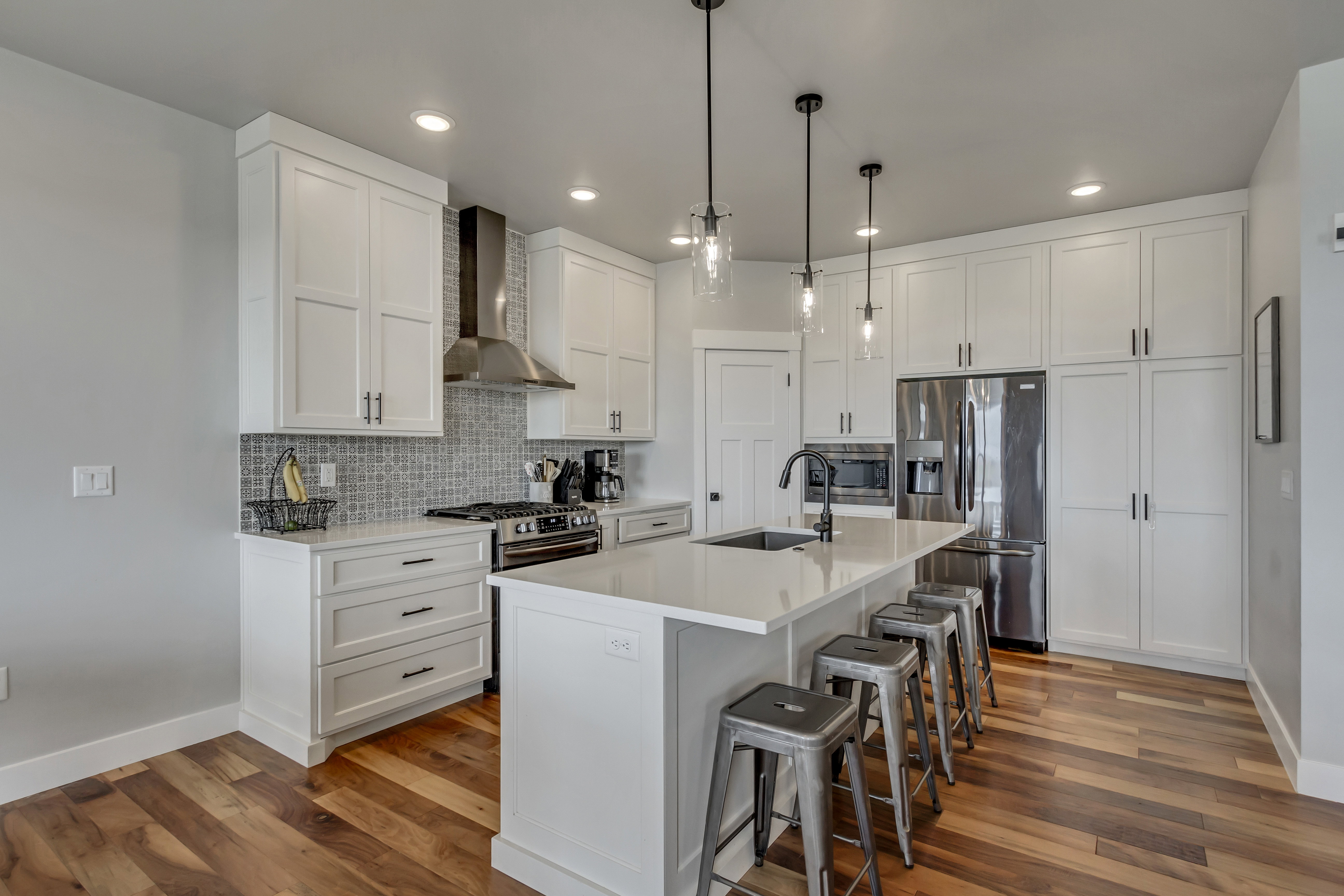 Modern kitchen featuring white cabinetry, stainless steel appliances, a white island with seating, pendant lighting, and wood-finish flooring