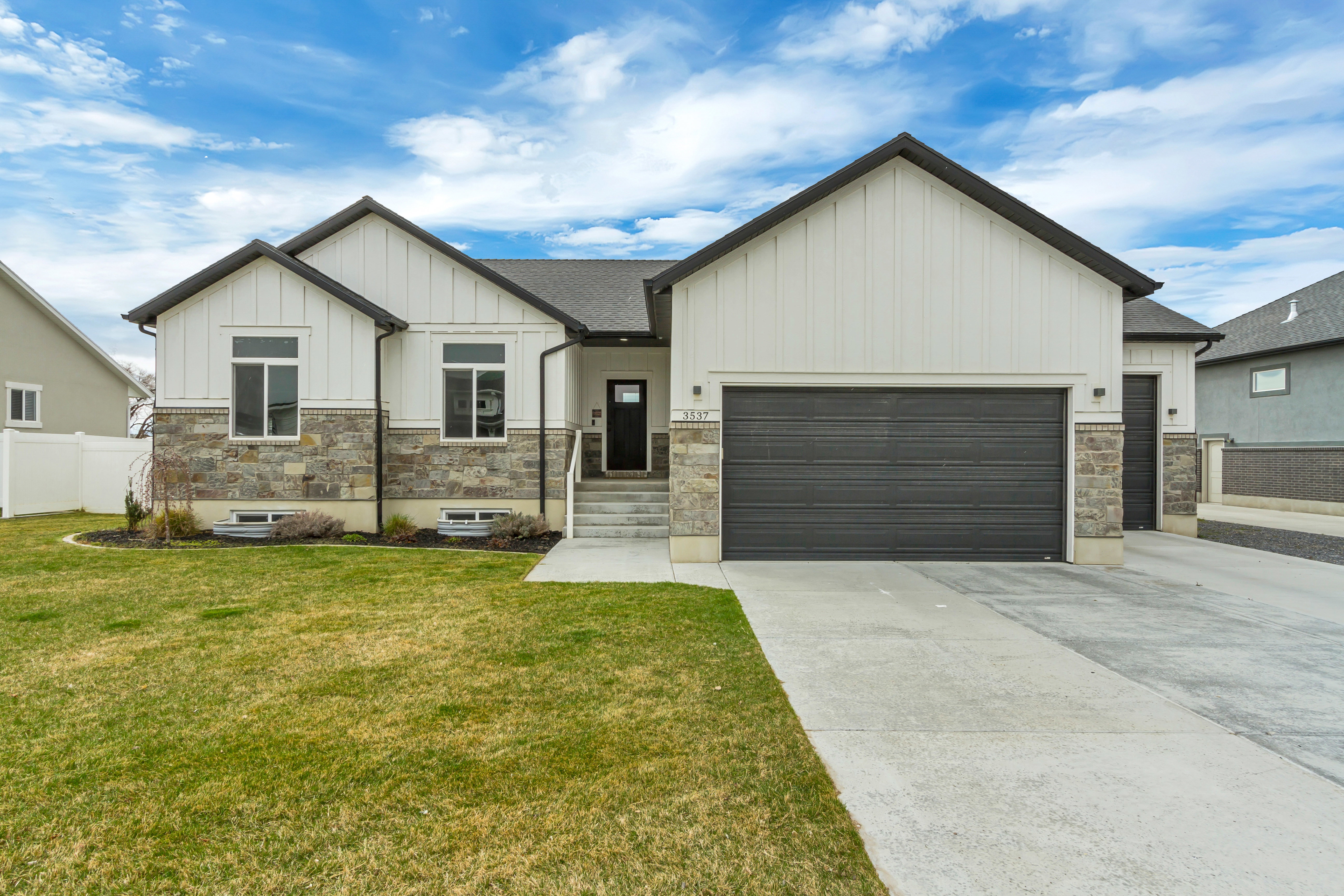 Contemporary residence featuring board and batten siding, stone veneer accents, an attached two-car garage, a covered entryway, and a concrete driveway