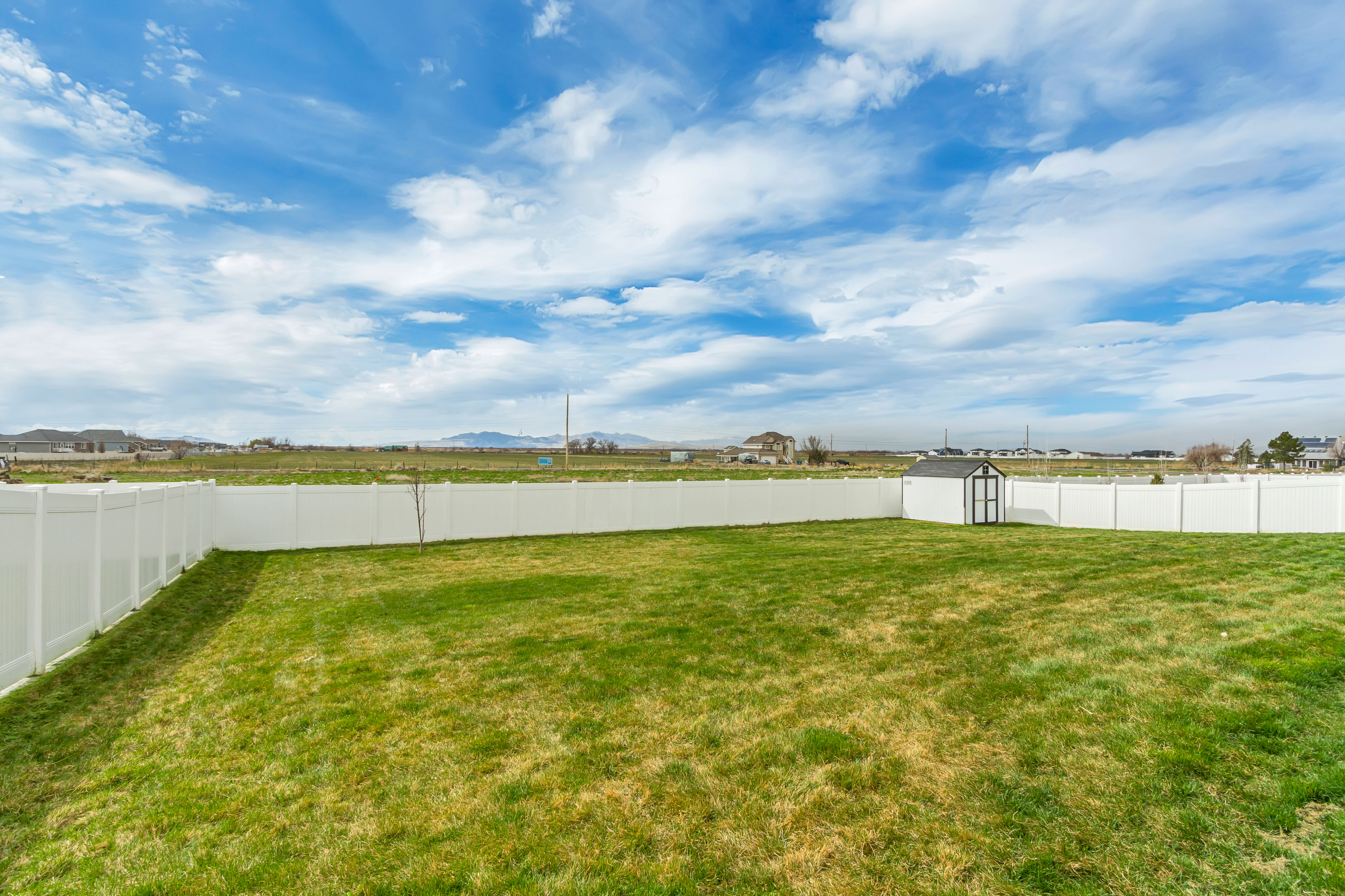 Expansive backyard featuring a green lawn, full perimeter white privacy fencing, and a black and white storage shed