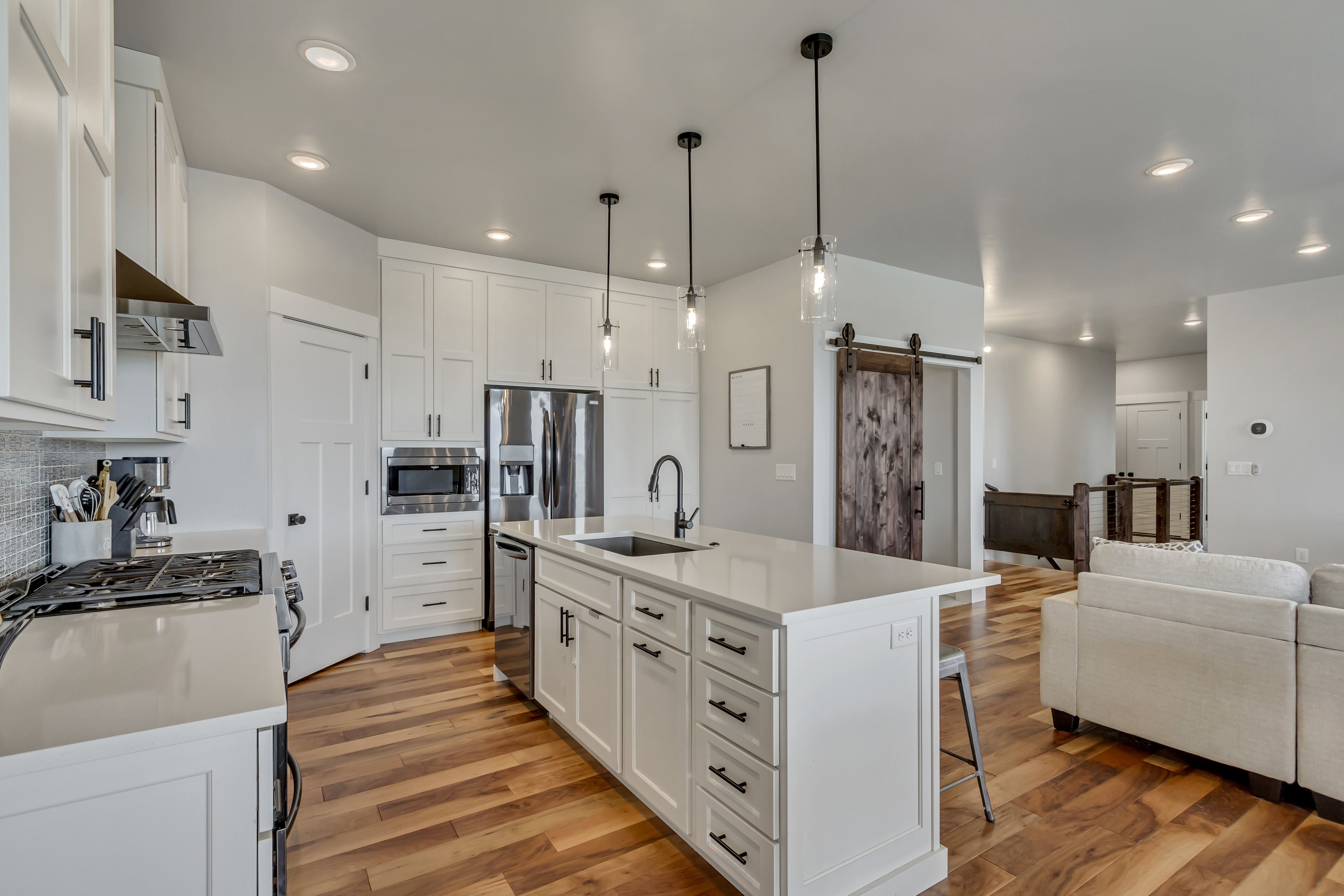 Modern kitchen featuring an expansive center island with seating, stainless steel appliances, white cabinetry, wood-finish flooring, and recessed lighting