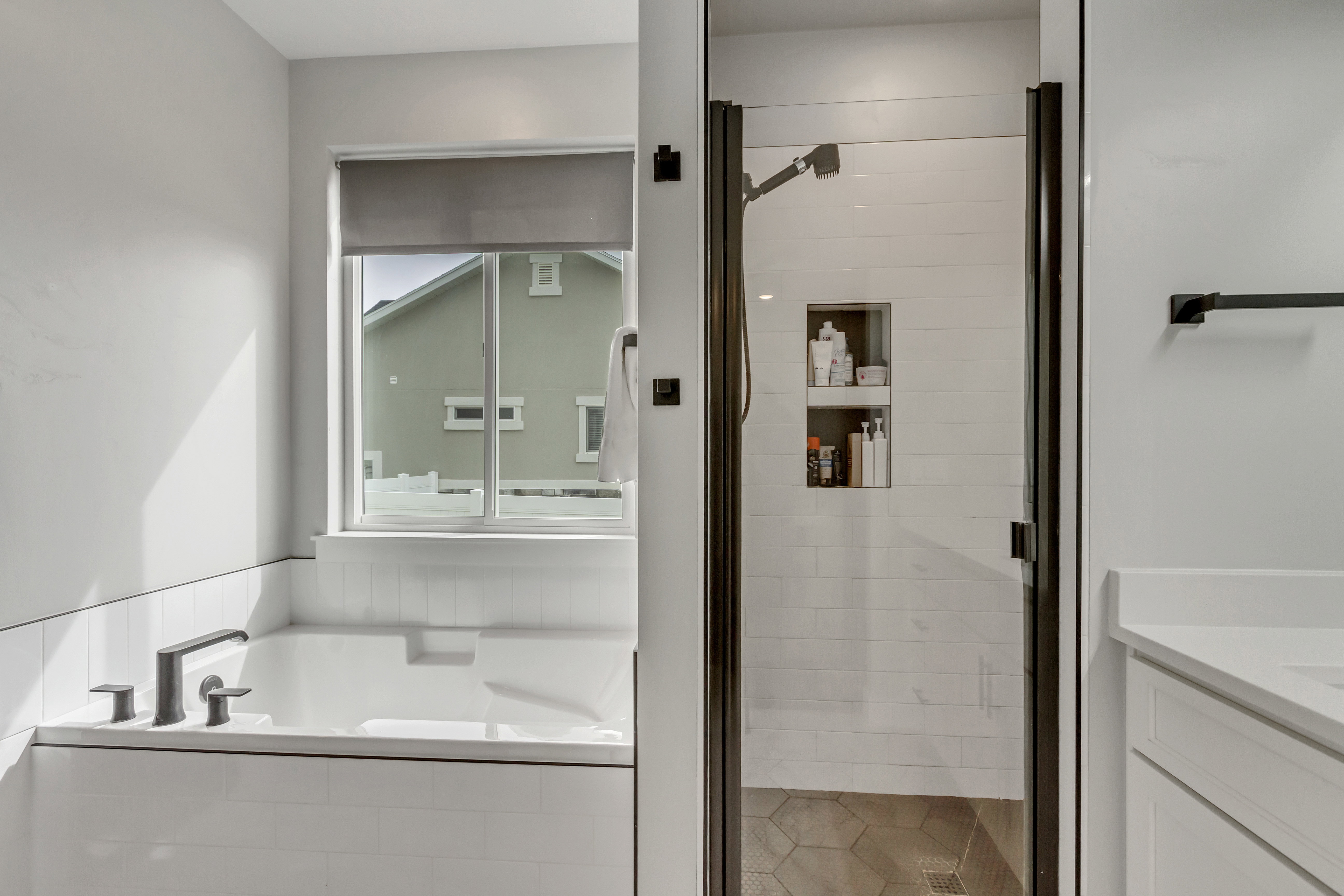 White tiled tub surround featuring a matte black deck-mounted faucet