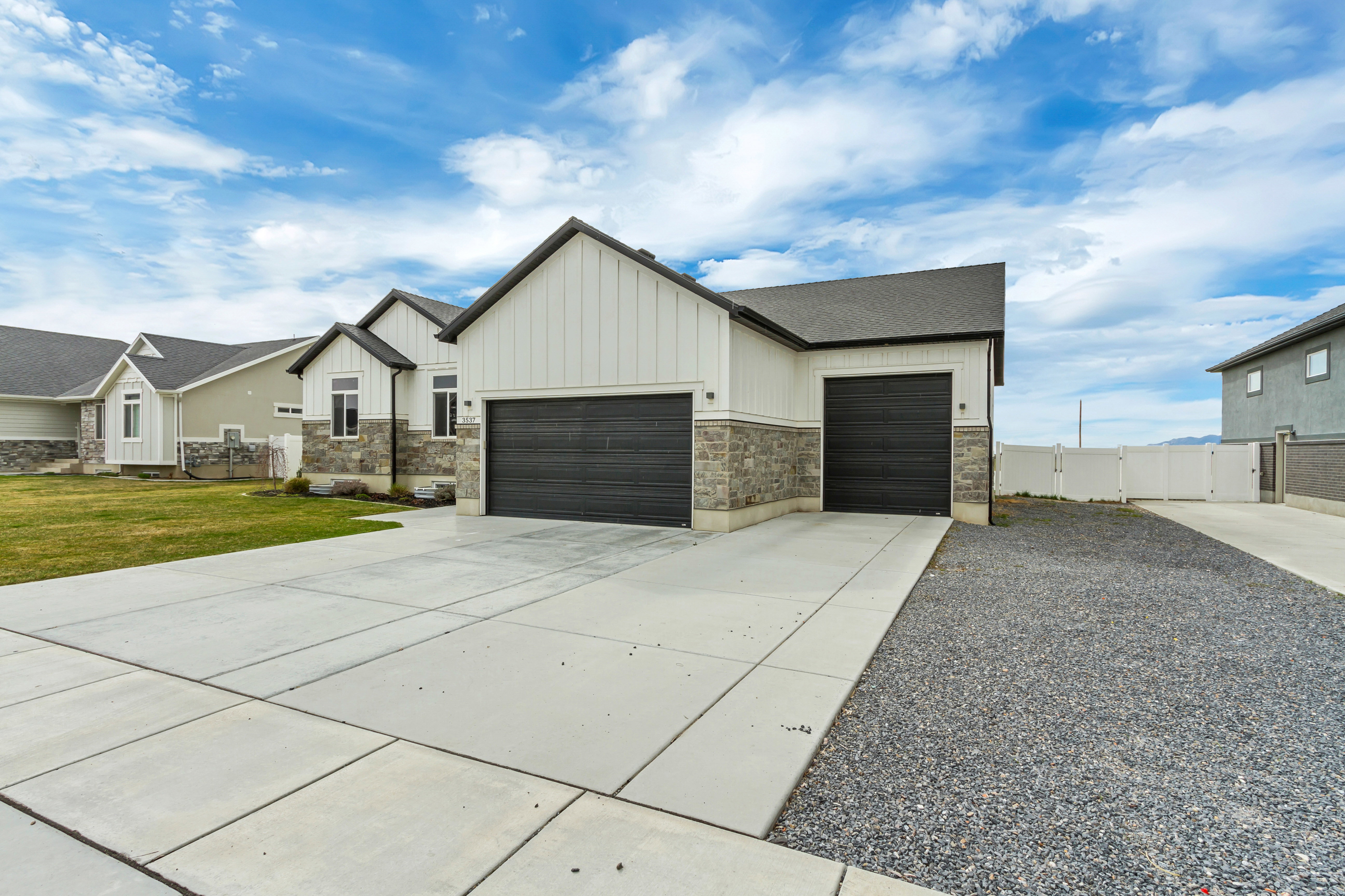 Contemporary exterior featuring board and batten siding, stone veneer accents, a dark asphalt shingle roof, and two dark garage doors