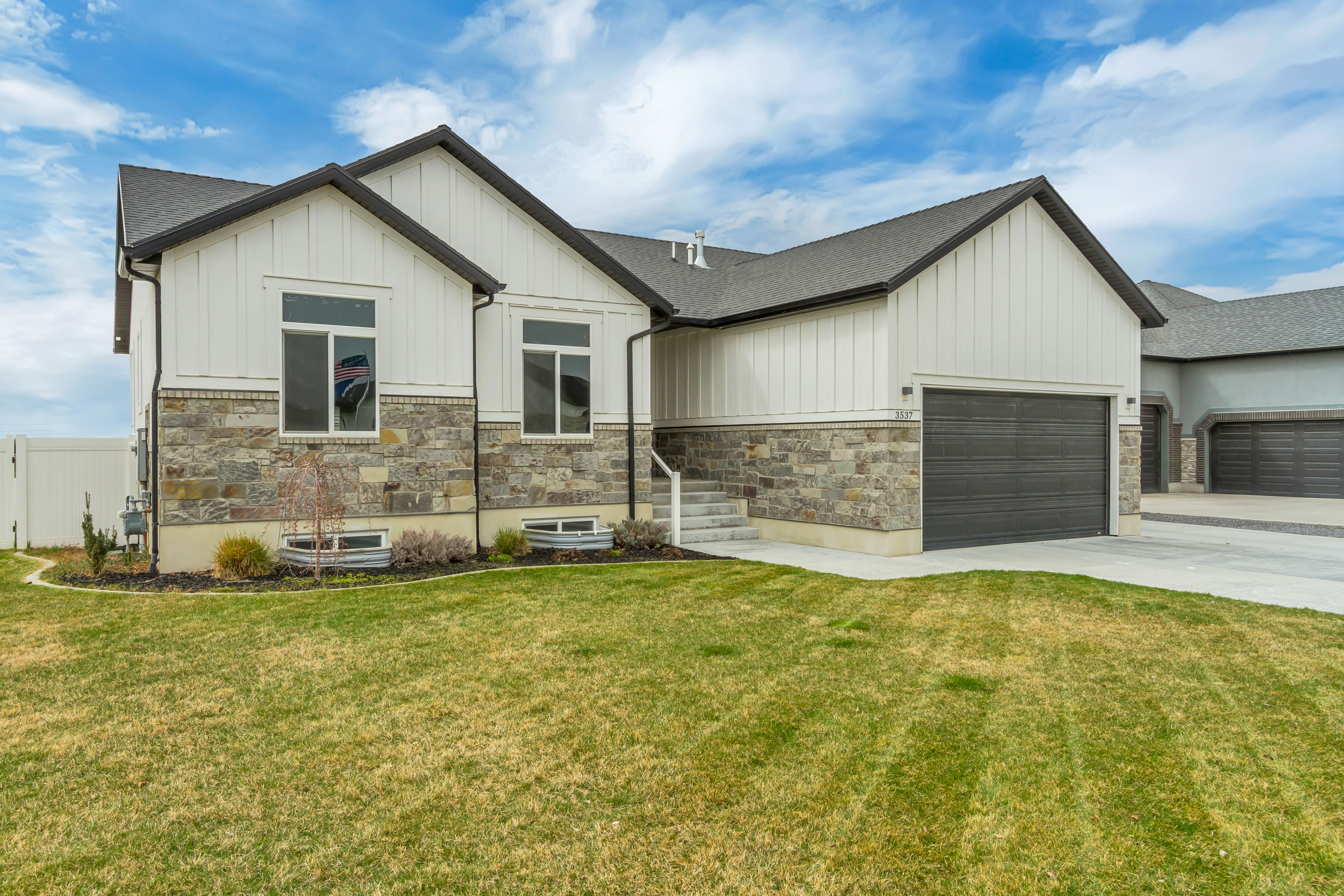 Contemporary residence featuring a two-car garage with a dark gray door, a stone and board-and-batten facade, and a dark shingle roof