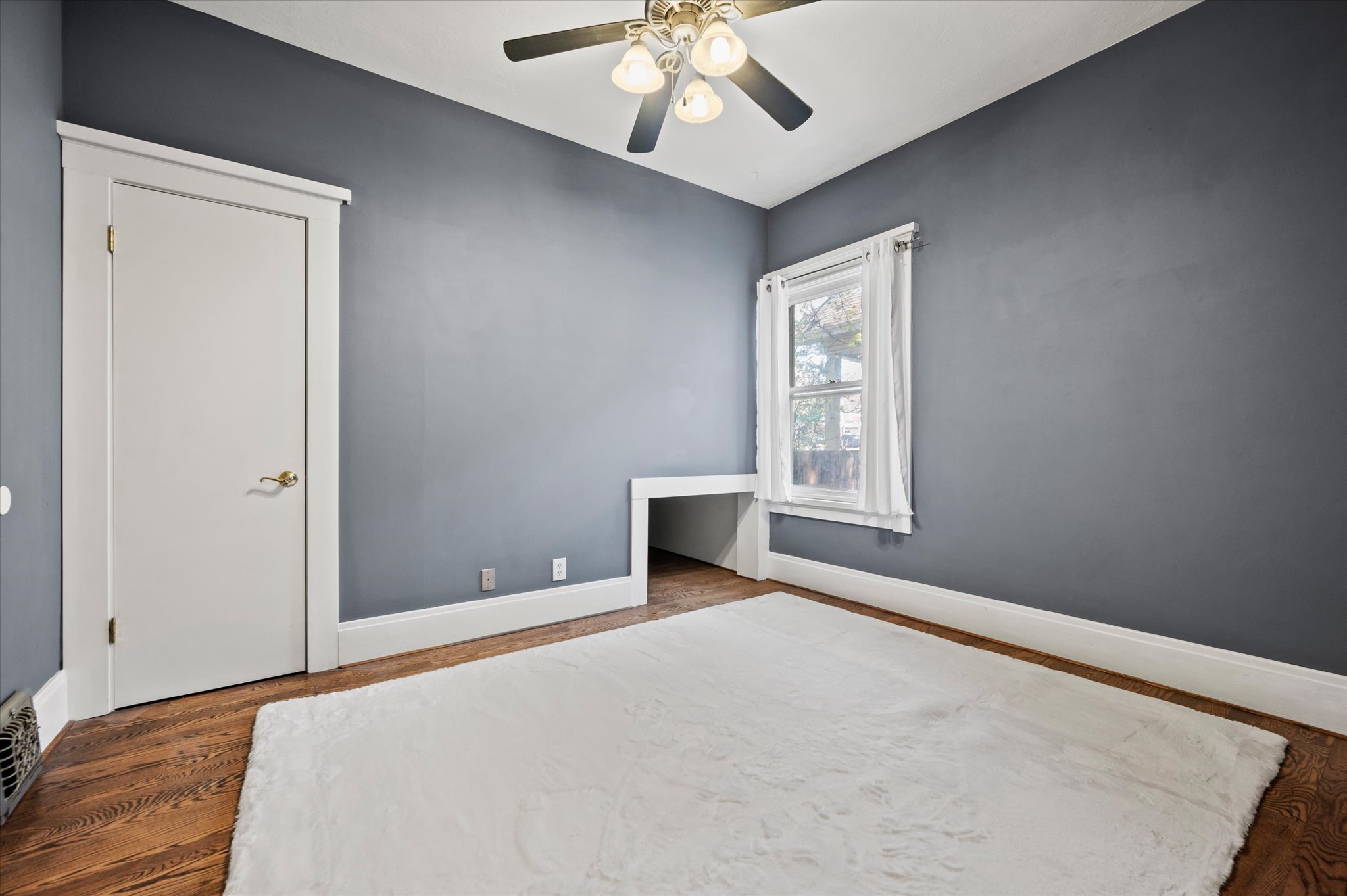 Room featuring dark gray walls, wood-finish flooring, a white trim door, and a built-in alcove