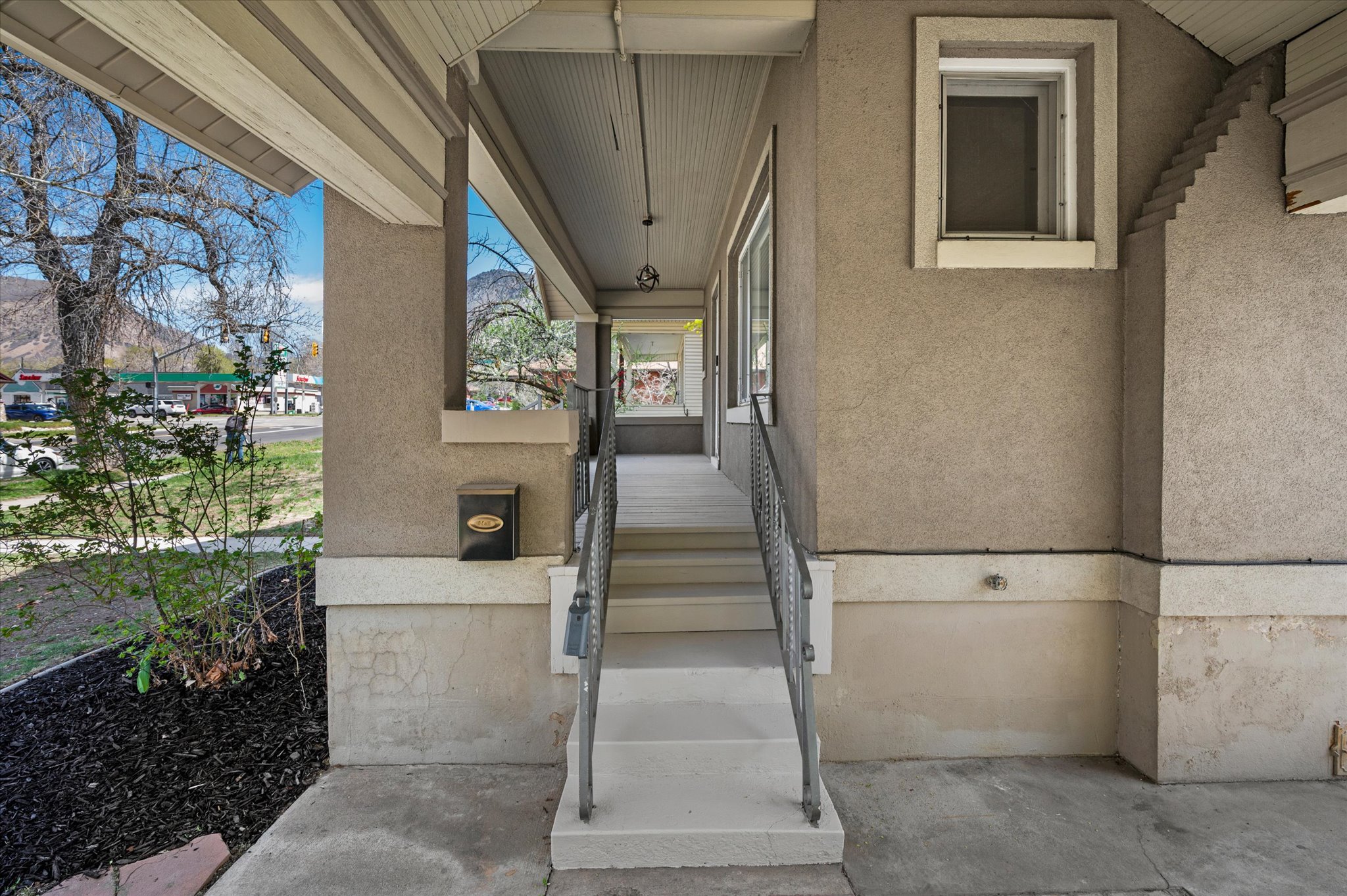 Covered porch entry featuring a stucco exterior, concrete steps, wrought iron railing, and decorative window trim
