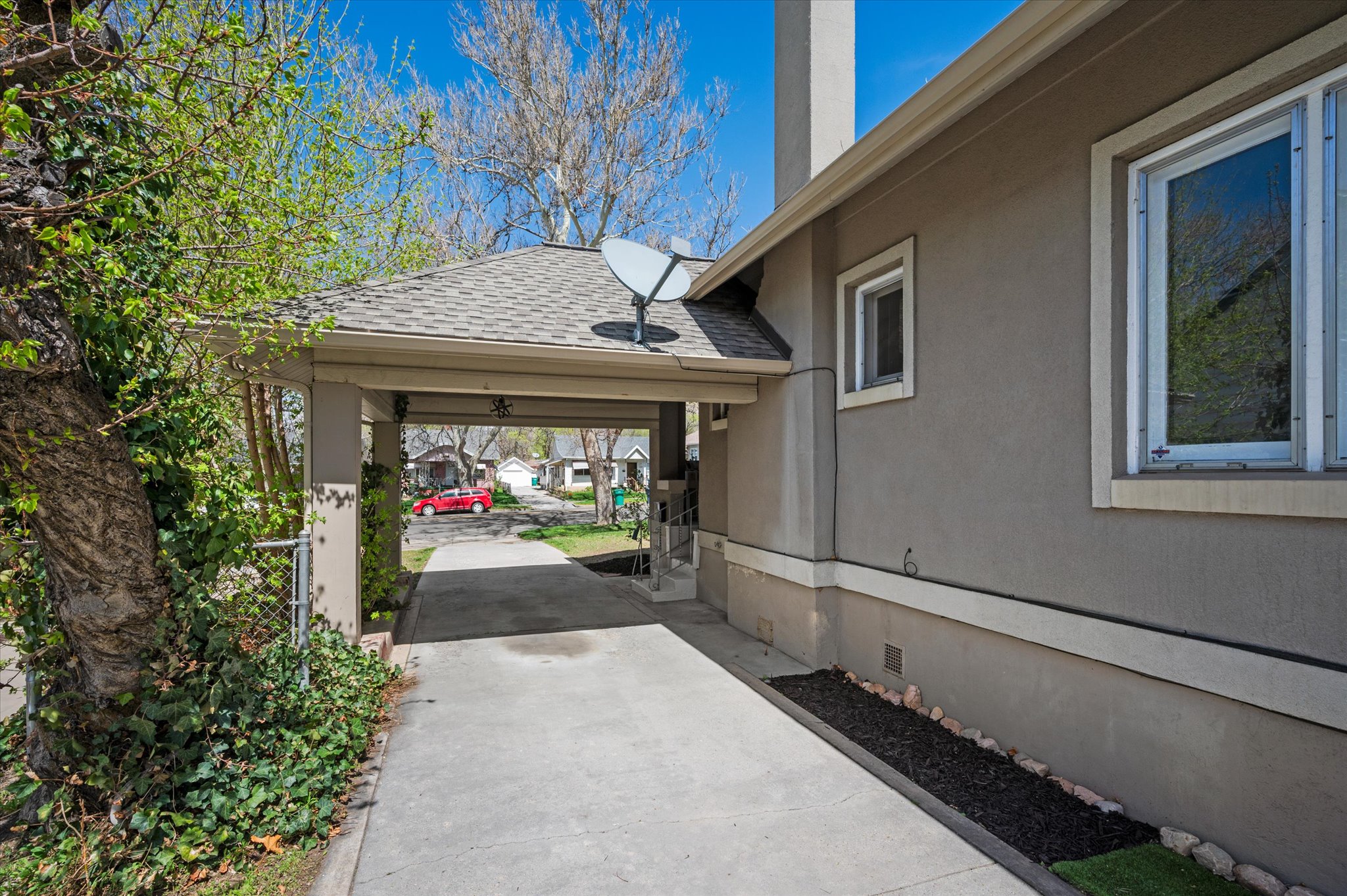 Covered carport entry with a shingle roof and stucco exterior