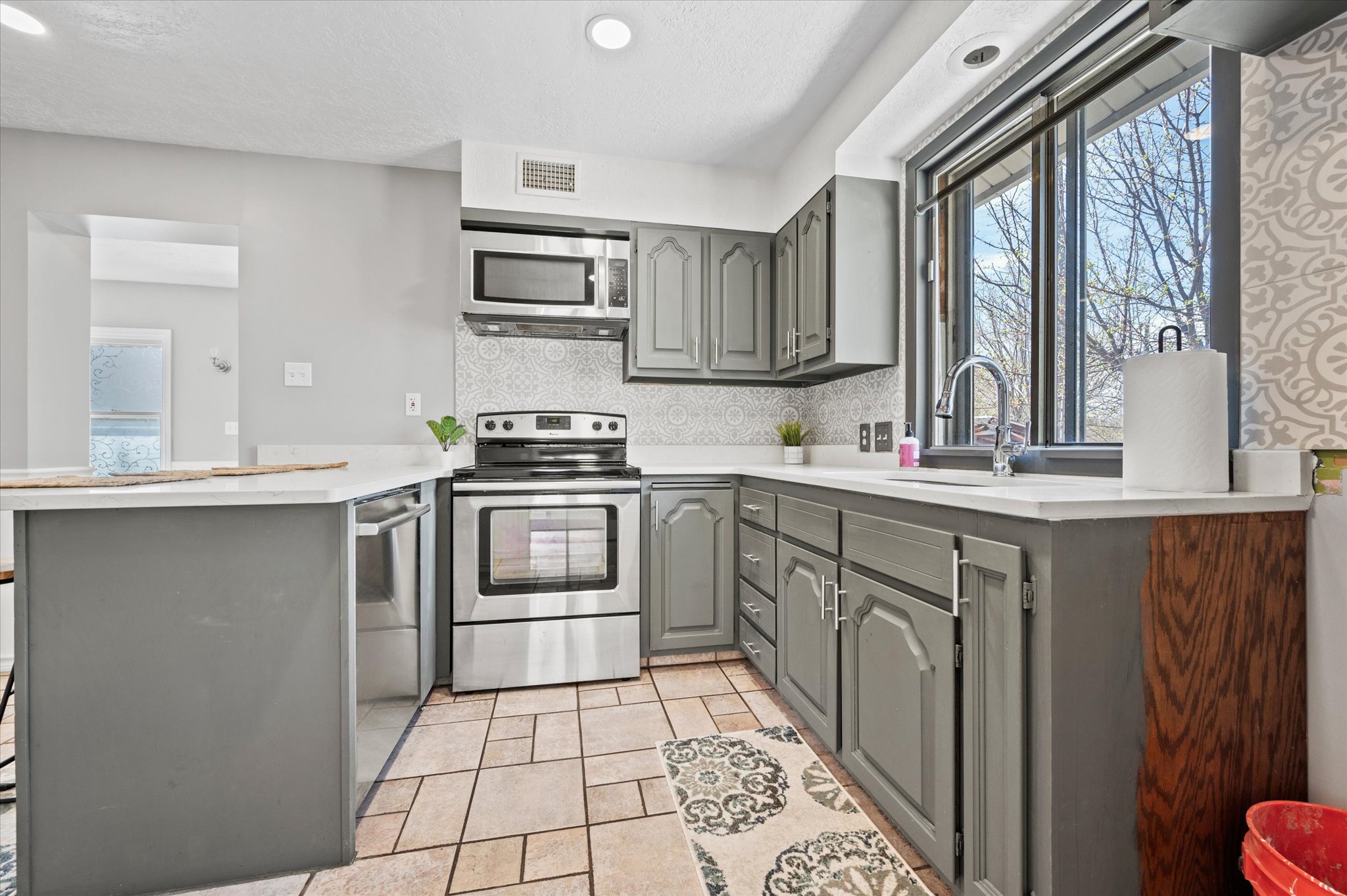 Kitchen featuring grey cabinetry, stainless steel appliances, white countertops, tile flooring, and a patterned tile backsplash